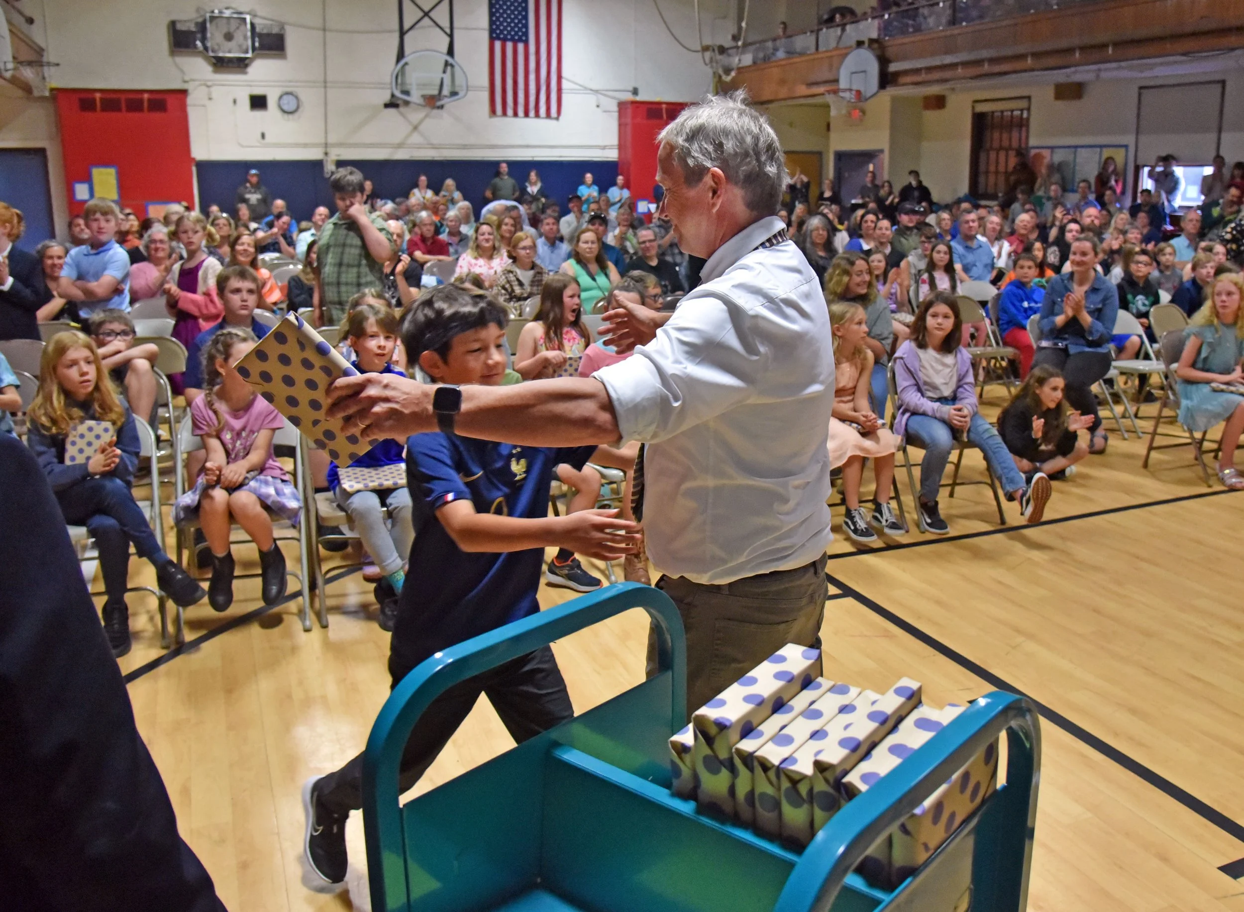 In a school tradition, Chris Costello hands out books to 2023 graduating 4th graders along with a hug. Photo by Gordon Miller