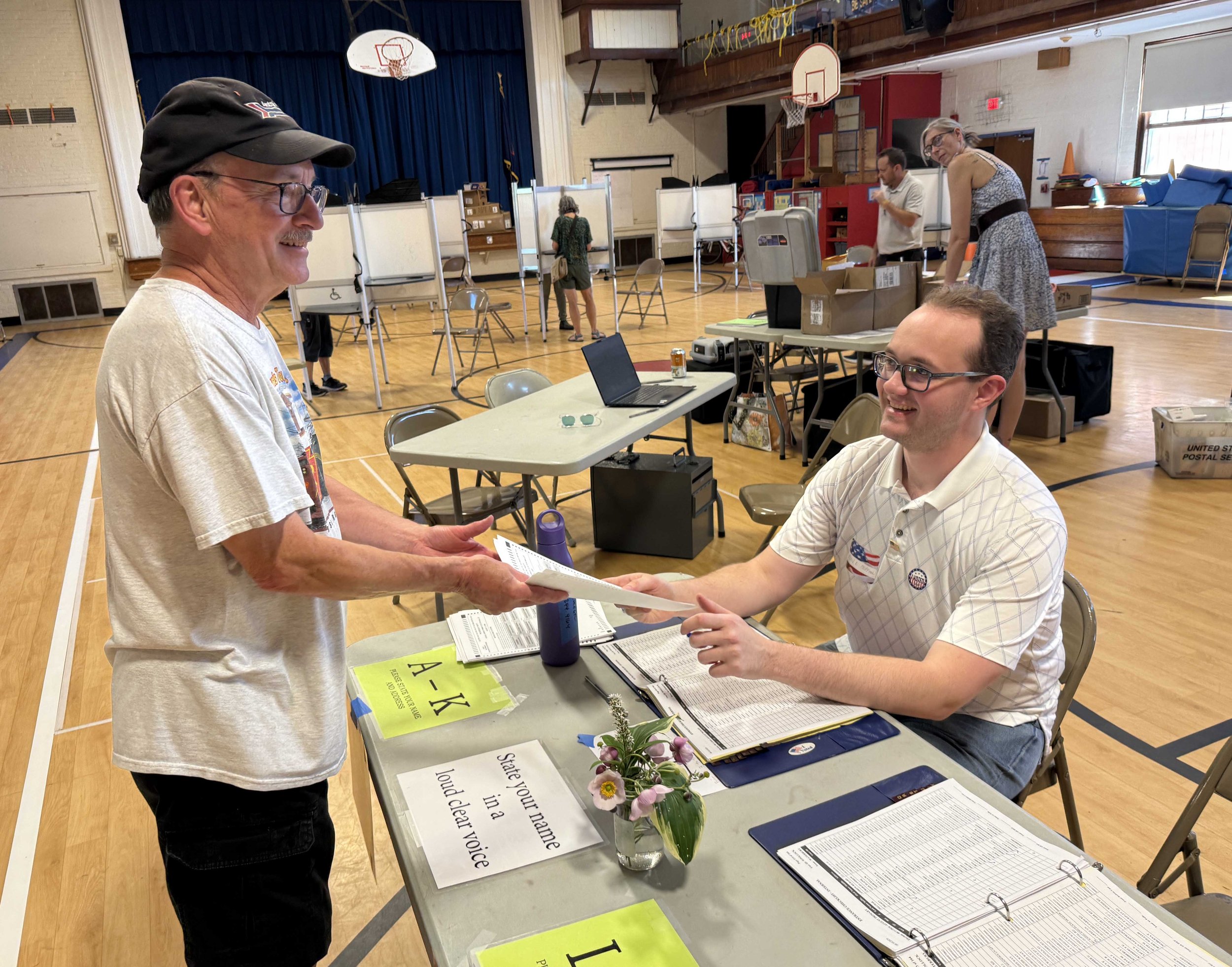   Voter Jim Hoffman checks in to get his ballots from son and Waterbury Select Board member Evan Hoffman. The younger Hoffman joined the board this spring, making him a member of the Board of Civil Authority and an elections official. Photo by Gordon