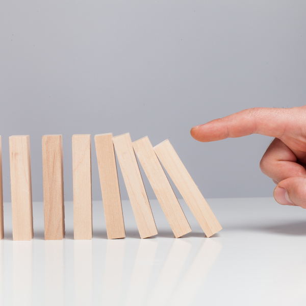 A hand about to knock over a row of falling wooden dominoes.