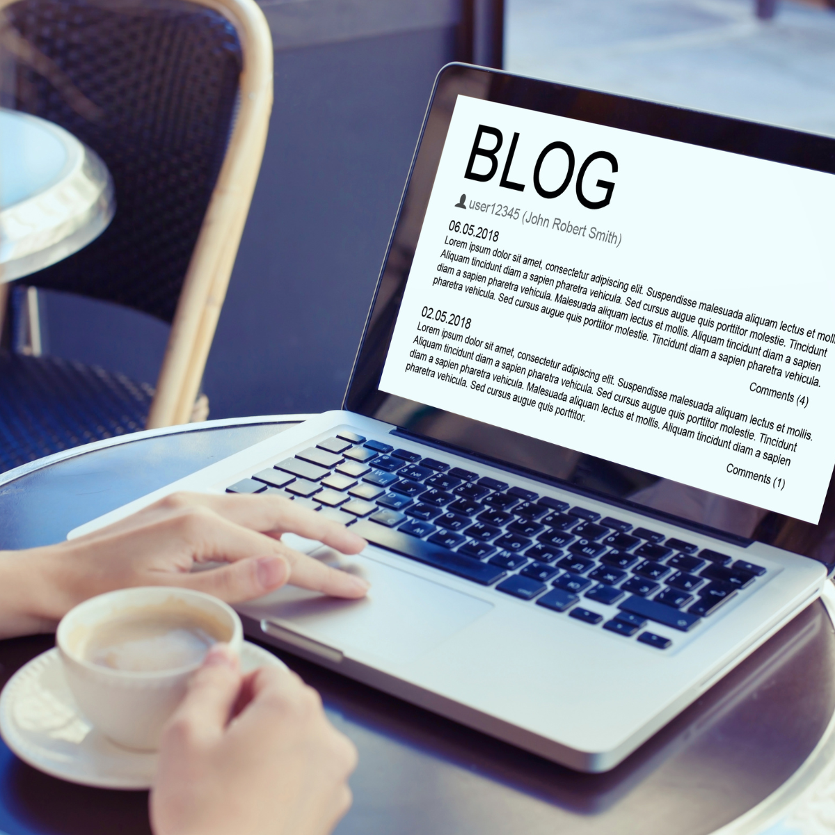 Open laptop on a round table with a person's hand holding a cup of coffee. The laptop screen displays a blog page with placeholder text.