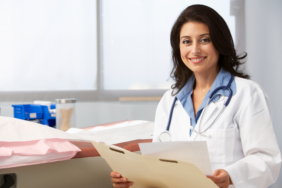 Female doctor in a white coat holding a clipboard with medical files, smiling.