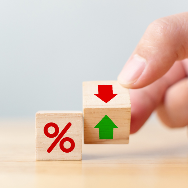 A person's hand is pushing a wooden block with a green upward arrow onto another wooden block with a red downward arrow, symbolizing changes in percentage or interest rates.