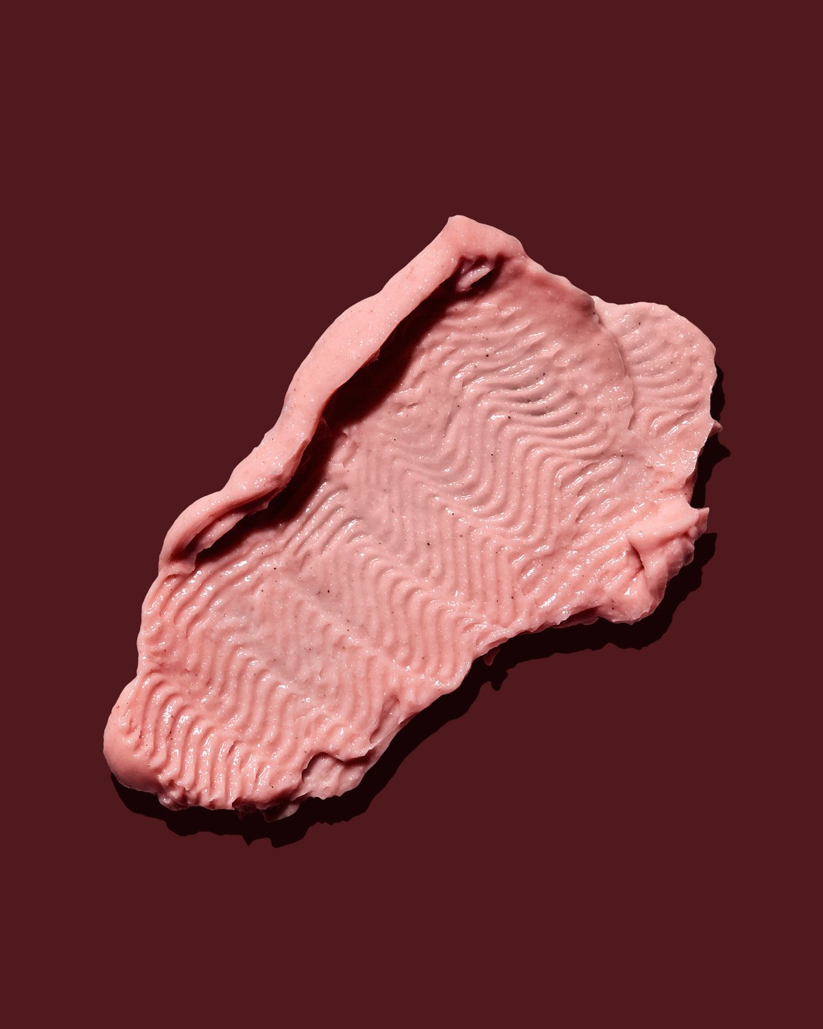 A swatch of pink face mask on dark cranberry background.