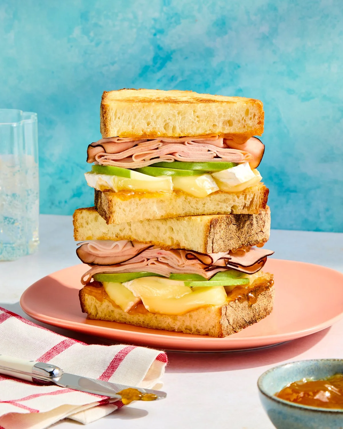 Ham, brie, and apple panini stacked on a colorful set for National Pork Board.