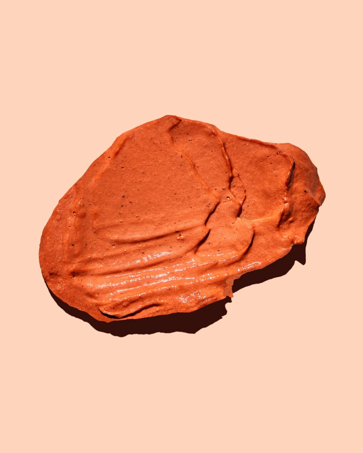 A swatch of reddish-brown face mask on a light orange background.