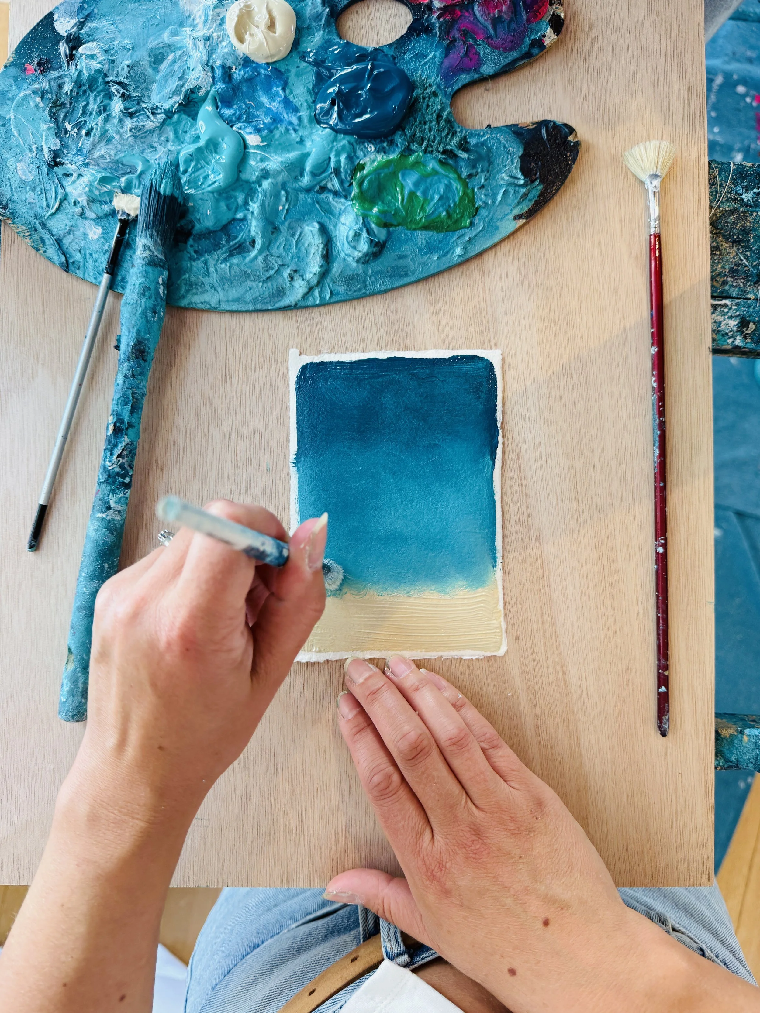 Gemma Lessinger painting a seascape scene onto a postcard