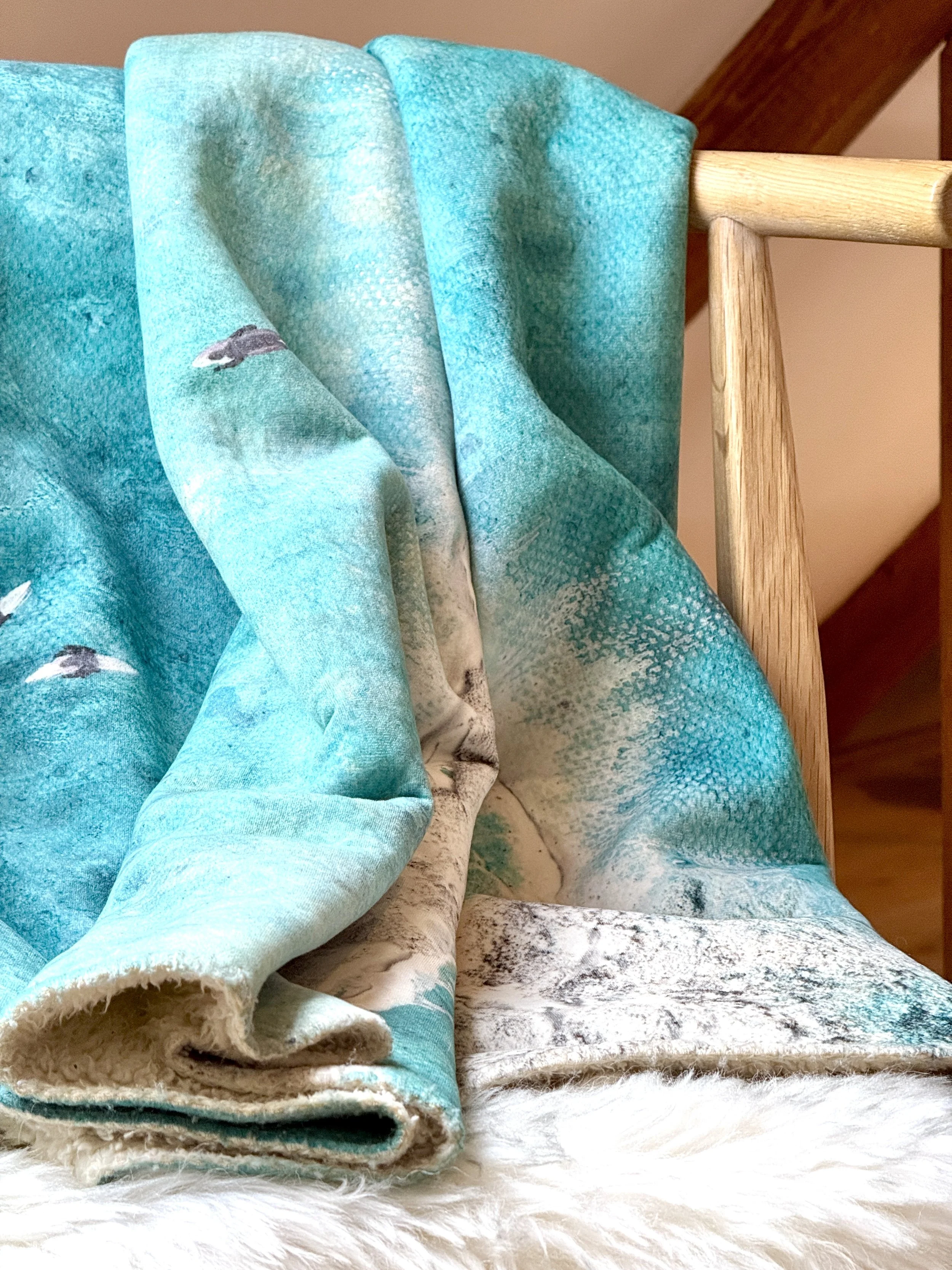 Detail of the Paddle Out blanket showing the surfers on surfboards motif against a textured ocean-blue background