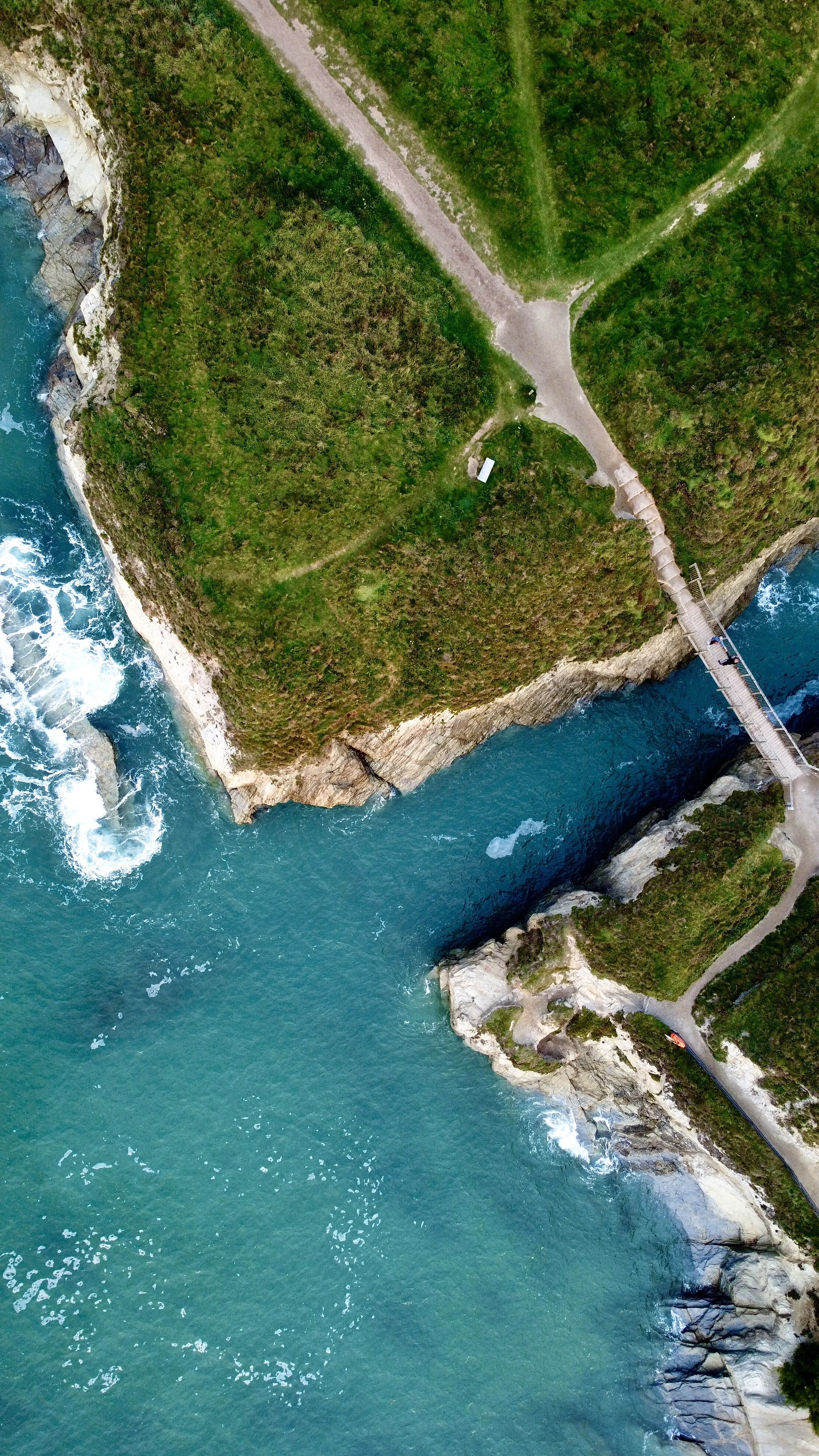 Aerial view of a coastal landscape with a river or creek flowing into the sea, surrounded by green vegetation and a bridge crossing over the water.
