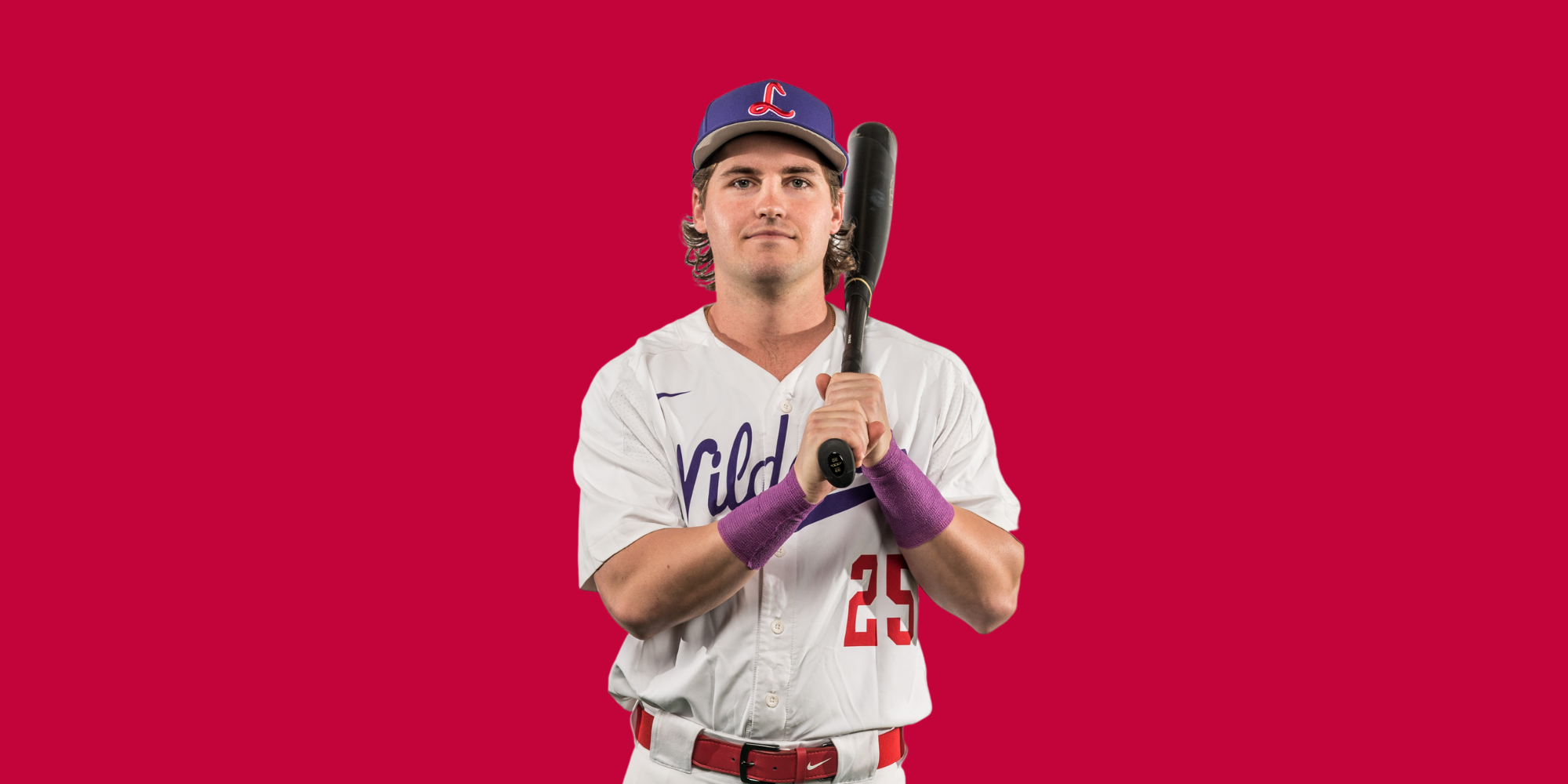 A young male baseball player dressed in a white uniform with purple wristbands and a blue cap with a red 'L' logo, holding a bat over his shoulder against a solid red background.