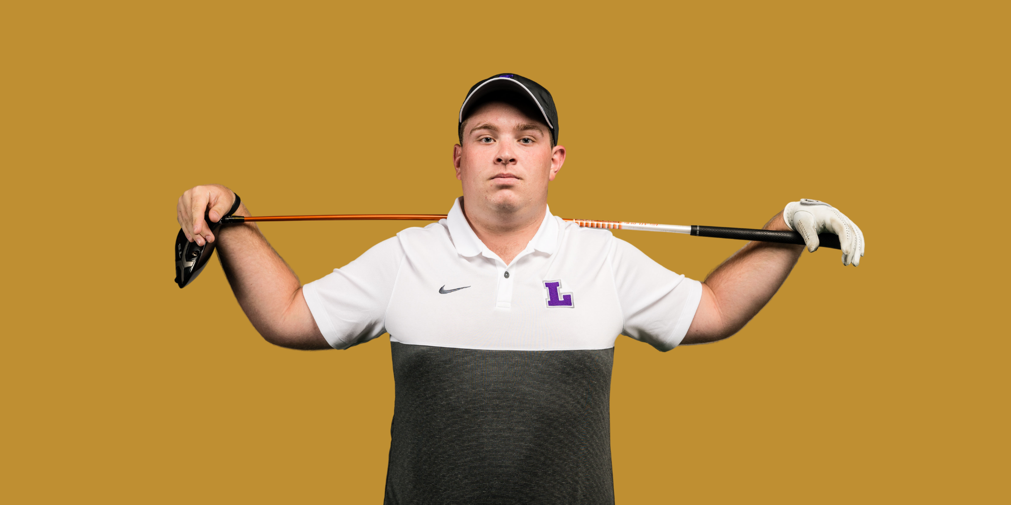 Young male golfer holding a golf club behind his shoulders, wearing a white polo shirt with a purple 'L' logo, a black cap, and a white glove on his left hand, standing against a mustard yellow background.