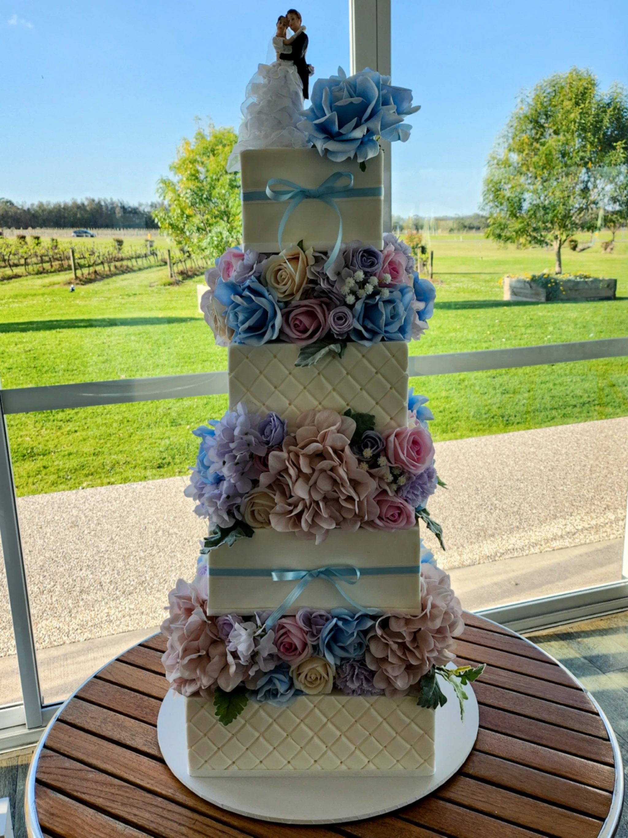 A pastel dream for Diorlouise &amp; Mark&rsquo;s special day 💙🍰

This towering 4-tier square cake was crafted in white chocolate with white chocolate ganache, wrapped in smooth fondant featuring two quilted tiers and soft baby blue ribbon accents f