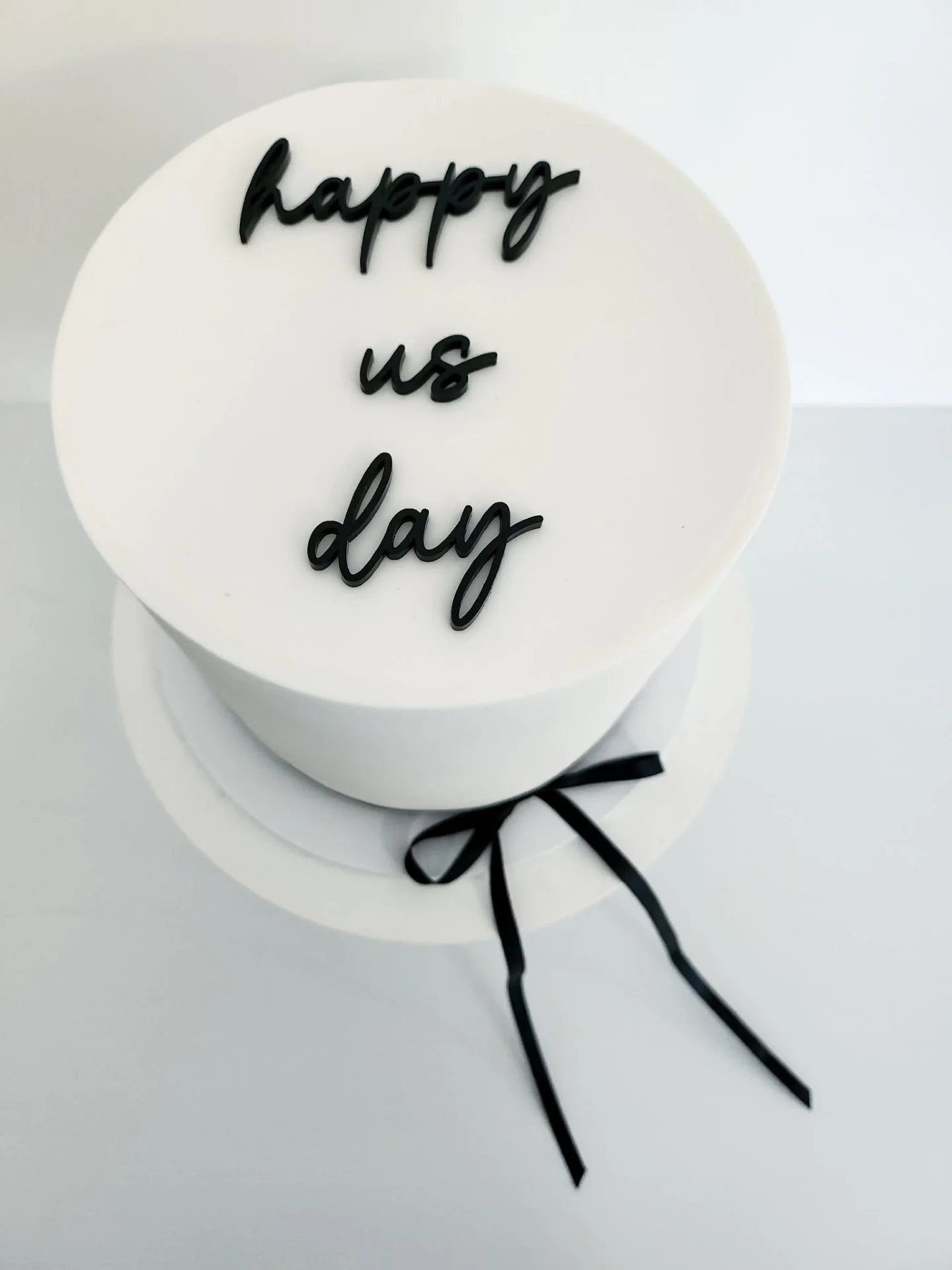 Happy Us Day 🖤

A sweet little celebration of love with layers of white chocolate raspberry, wrapped in smooth white fondant and finished with a long black ribbon bow, just like their wedding cake.

Topped with a simple black &ldquo;happy us day&rdq
