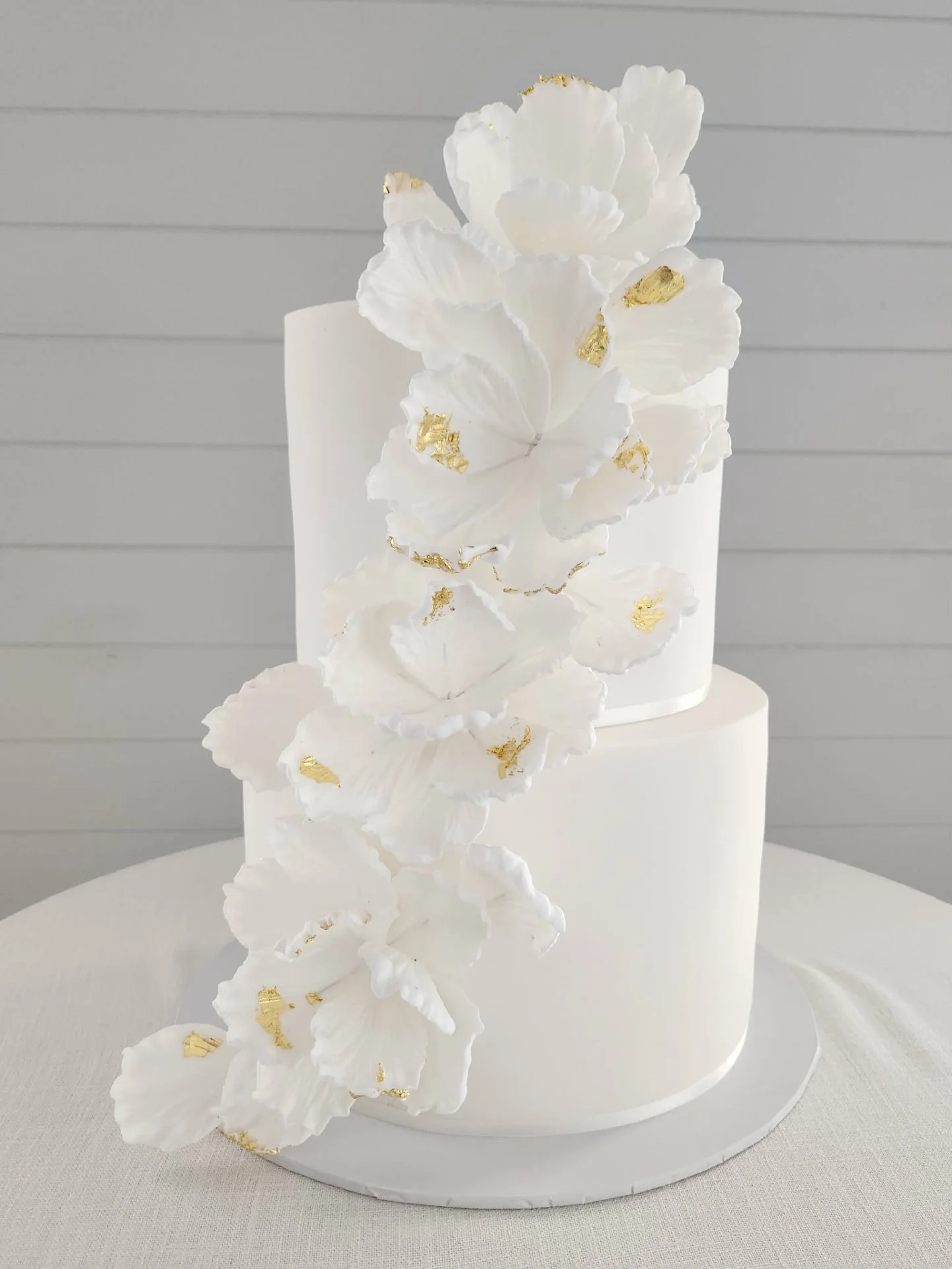 A romantic two-tier white fondant beauty layered with white chocolate raspberry and rich chocolate.

Finished with a deconstructed flower petal design and delicate gold leaf accents, this cake was the perfect blend of texture and elegance.✨

#dragonf