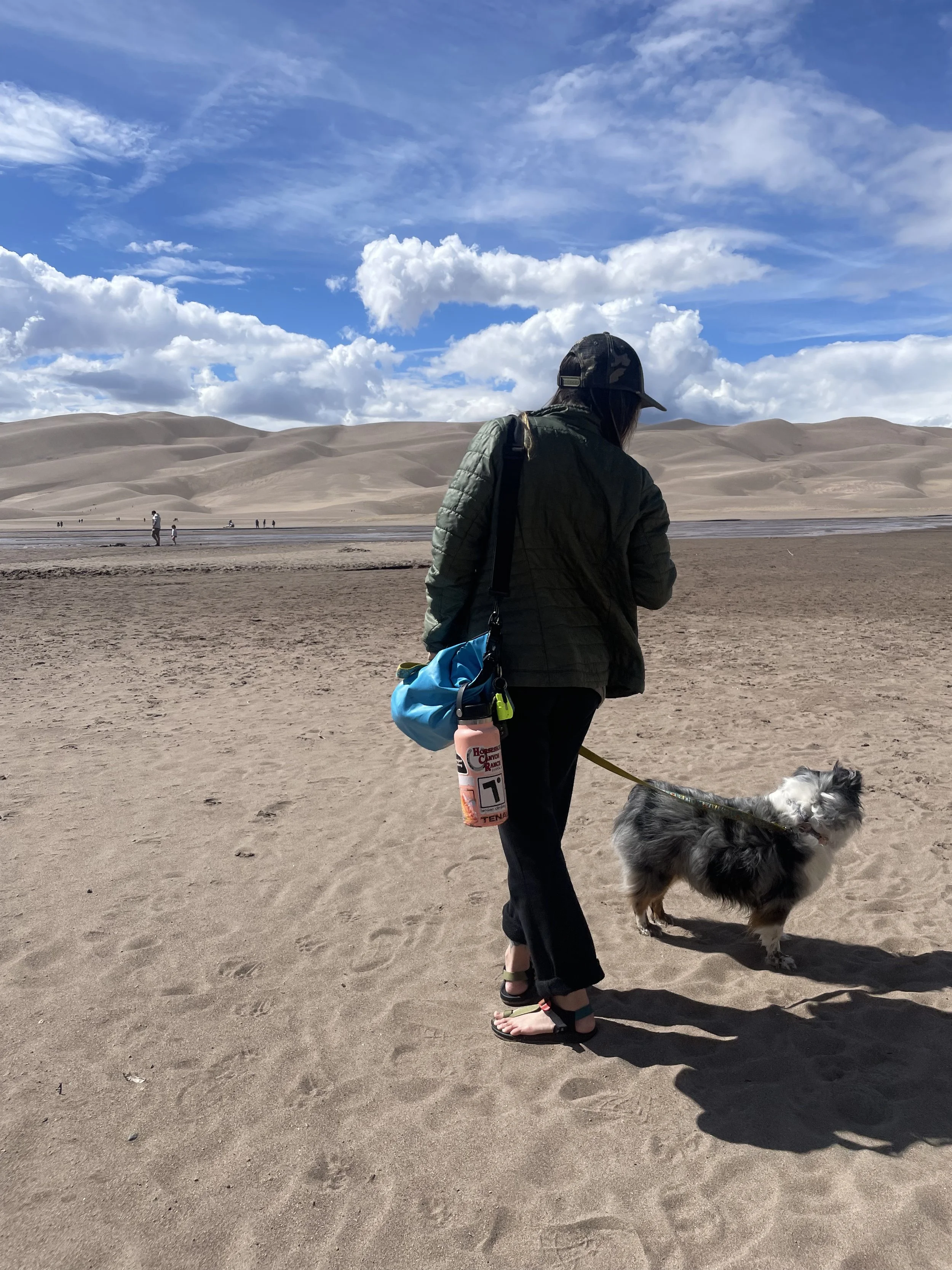 Female wellness, lifestyle, and outdoor industry copywriter stand at Great Sand Dunes National Park with mini aussie dog.