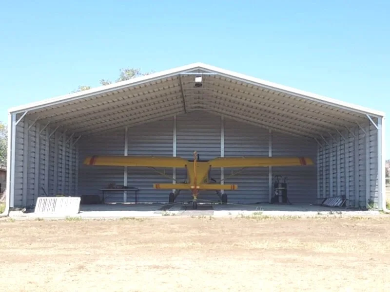 Yellow and red light aircraft inside a large open Shedfast shade shed hangar.