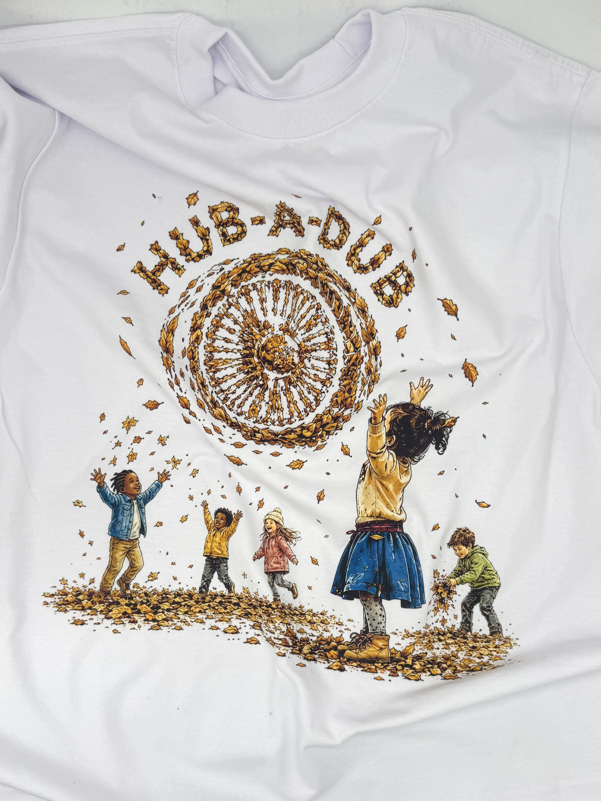 Close-up of the gold, orange and brown wheel-inspired graphic on the Hub-A-Dub Courtyard Falls white cropped tee