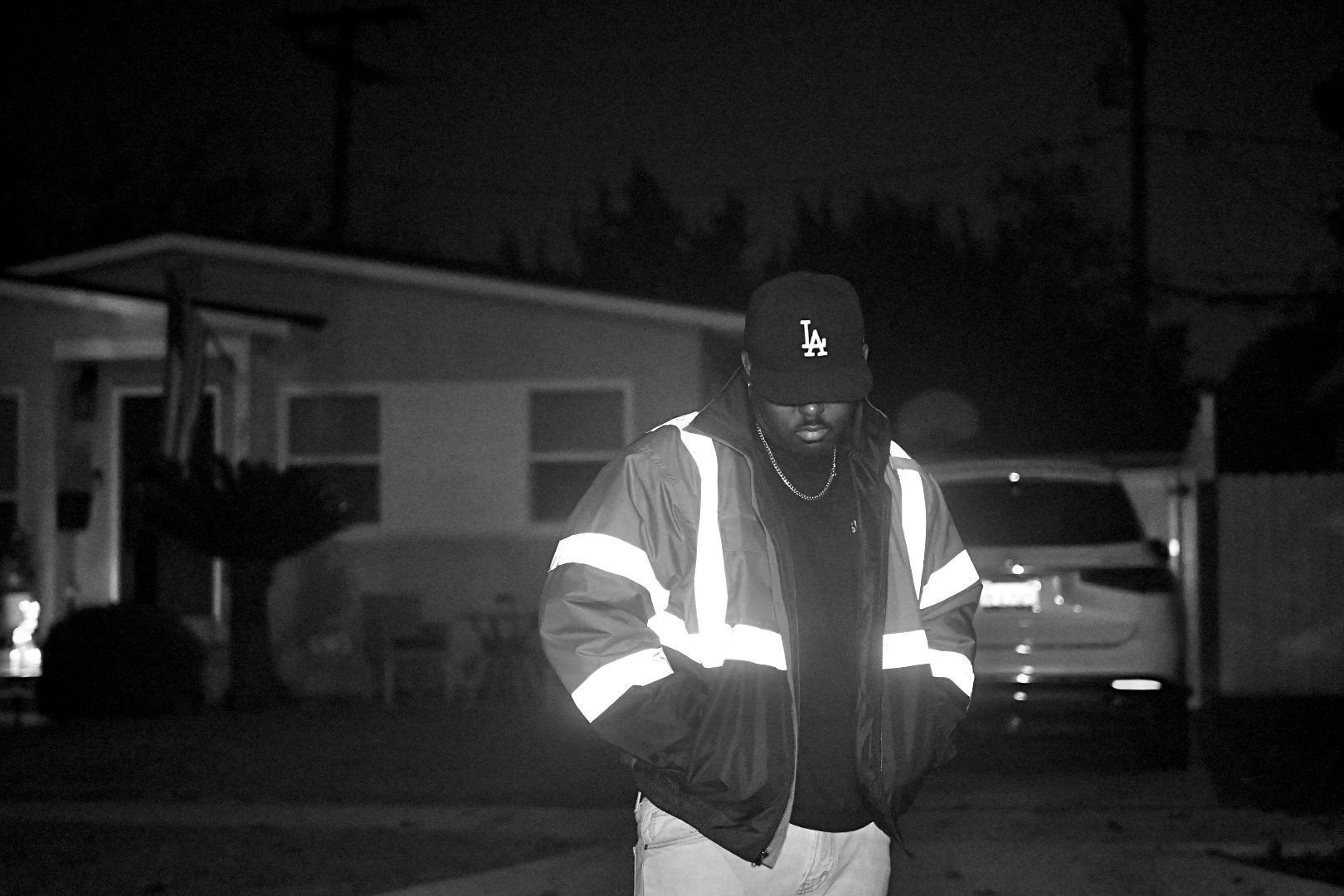 Compton artist Yestrdy photographed at night in Los Angeles wearing a reflective jacket in a cinematic black-and-white portrait.
