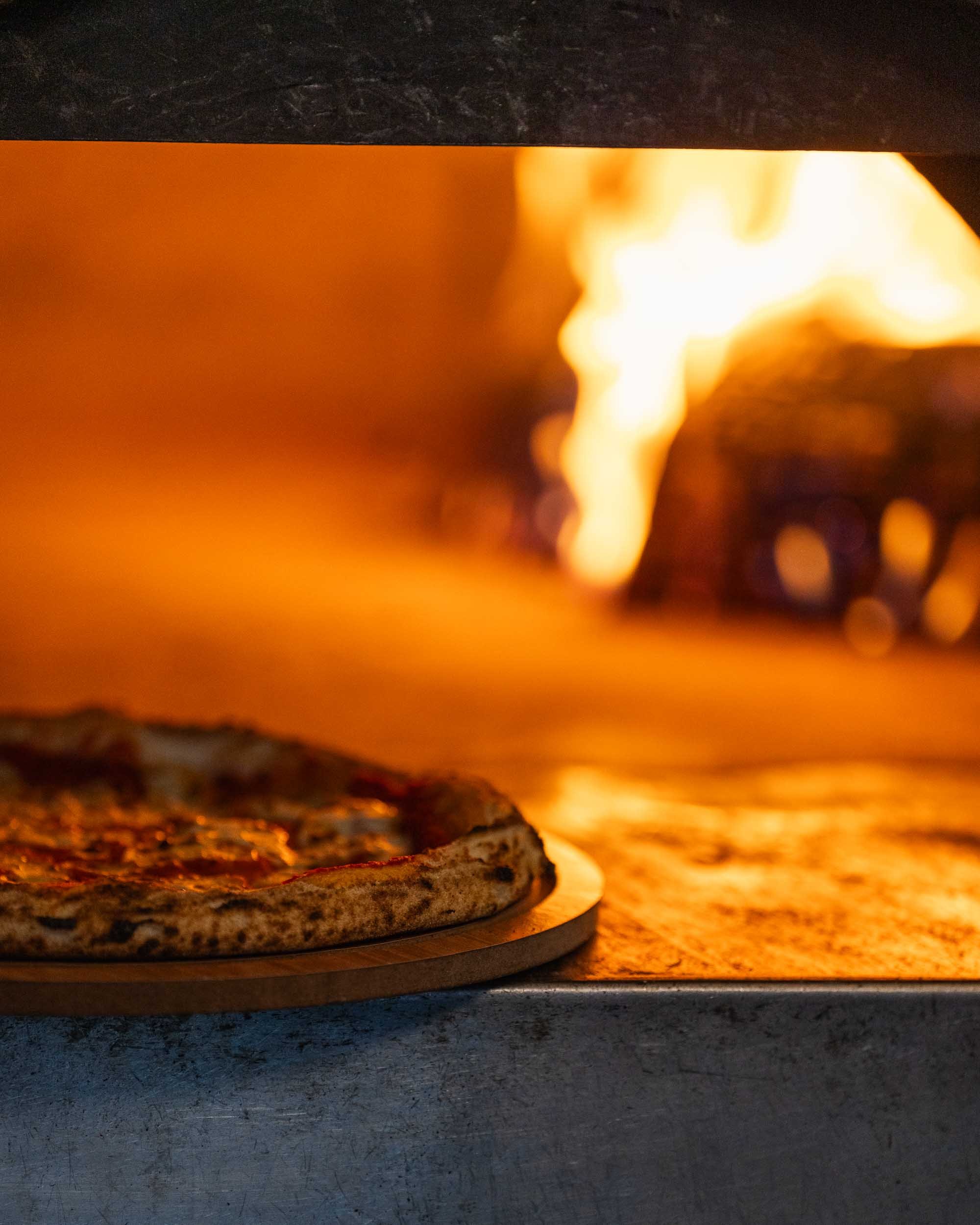 Close-up of a pizza cooking in an oven with flames visible in the background.