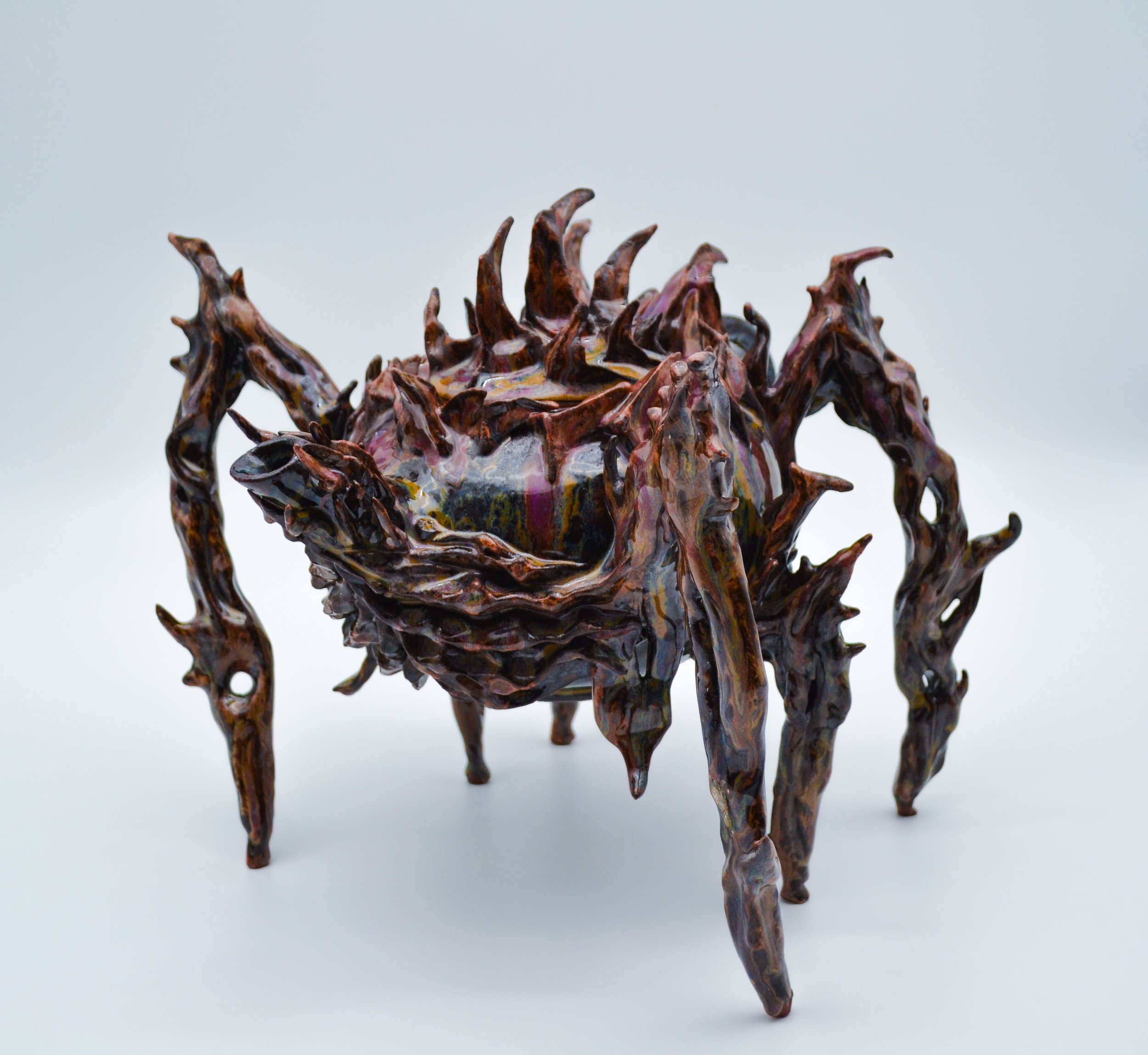 Close-up of an abstract sculpture resembling a spider made of brown speckled stoneware fired to cone 5 with pointed, irregular shapes against a plain white background by artist Allison Genereaux of Alcove Ceramics.