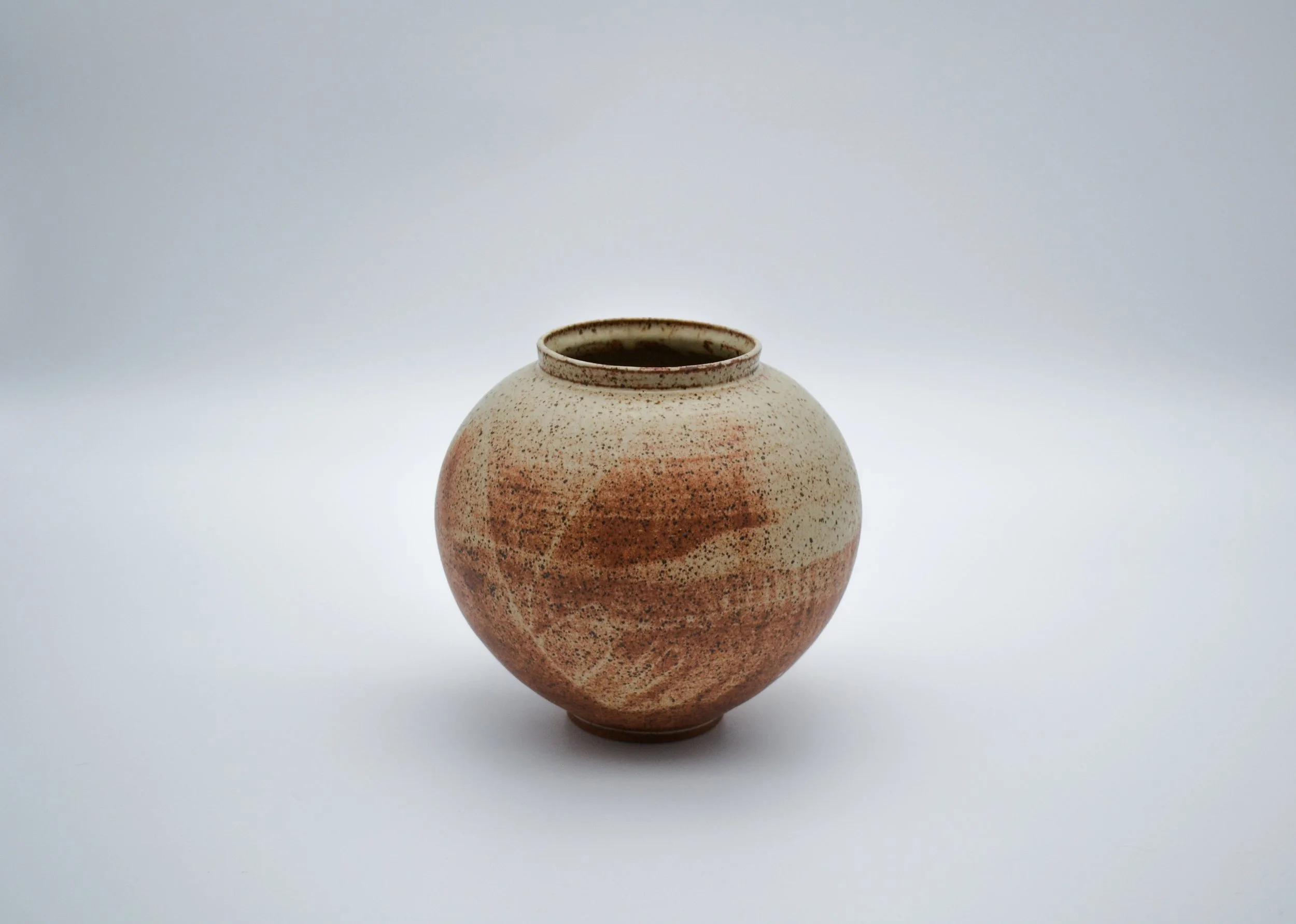 A round ceramic vase with a speckled beige and reddish-brown glaze, set against a plain white background made by artist Allison Genereaux of Alcove Ceramics.