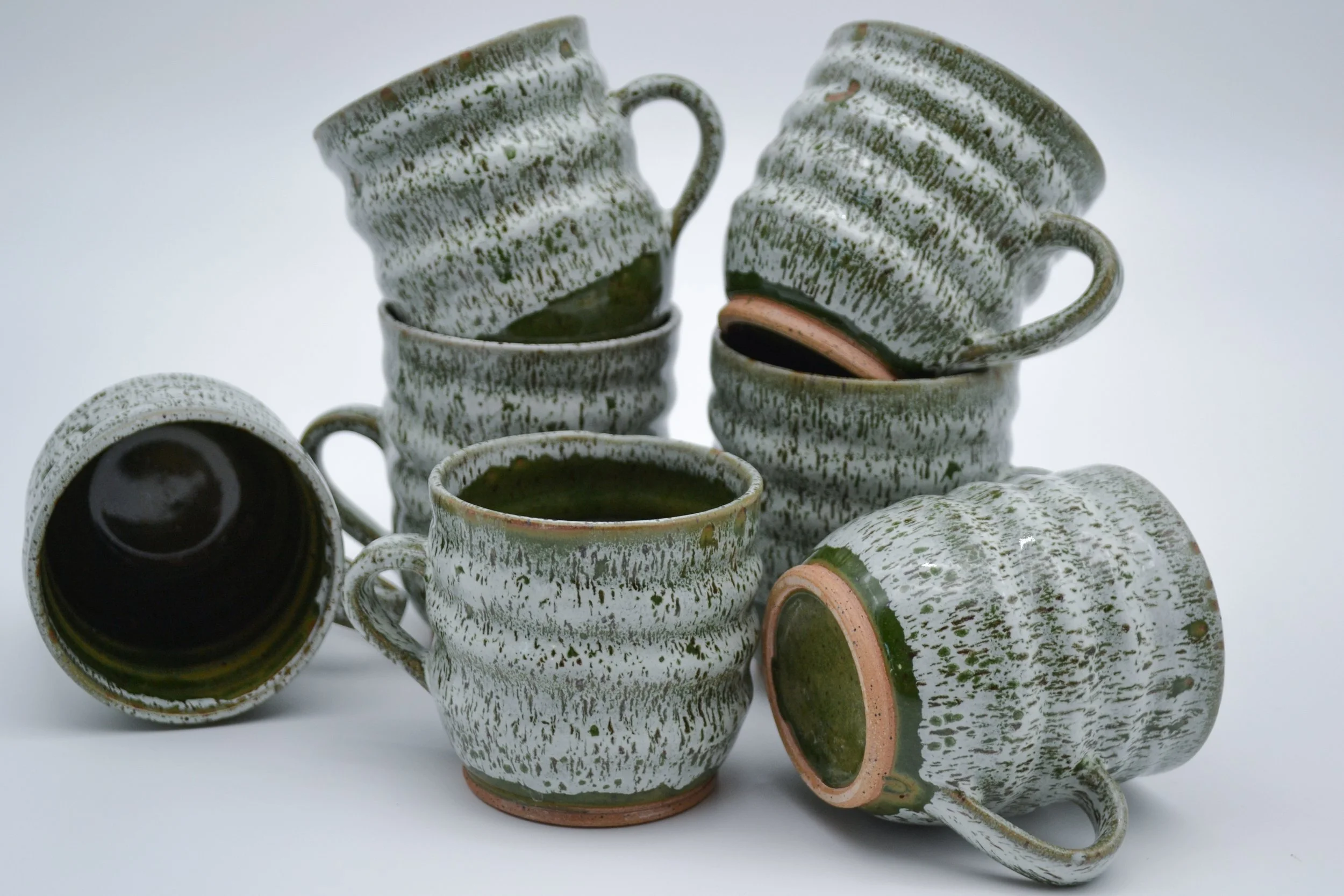 Stacked ceramic cups with a green and white speckled glaze on a white background, some cups are upside down showing the unglazed base made by artist Allison Genereaux of Alcove Ceramics.