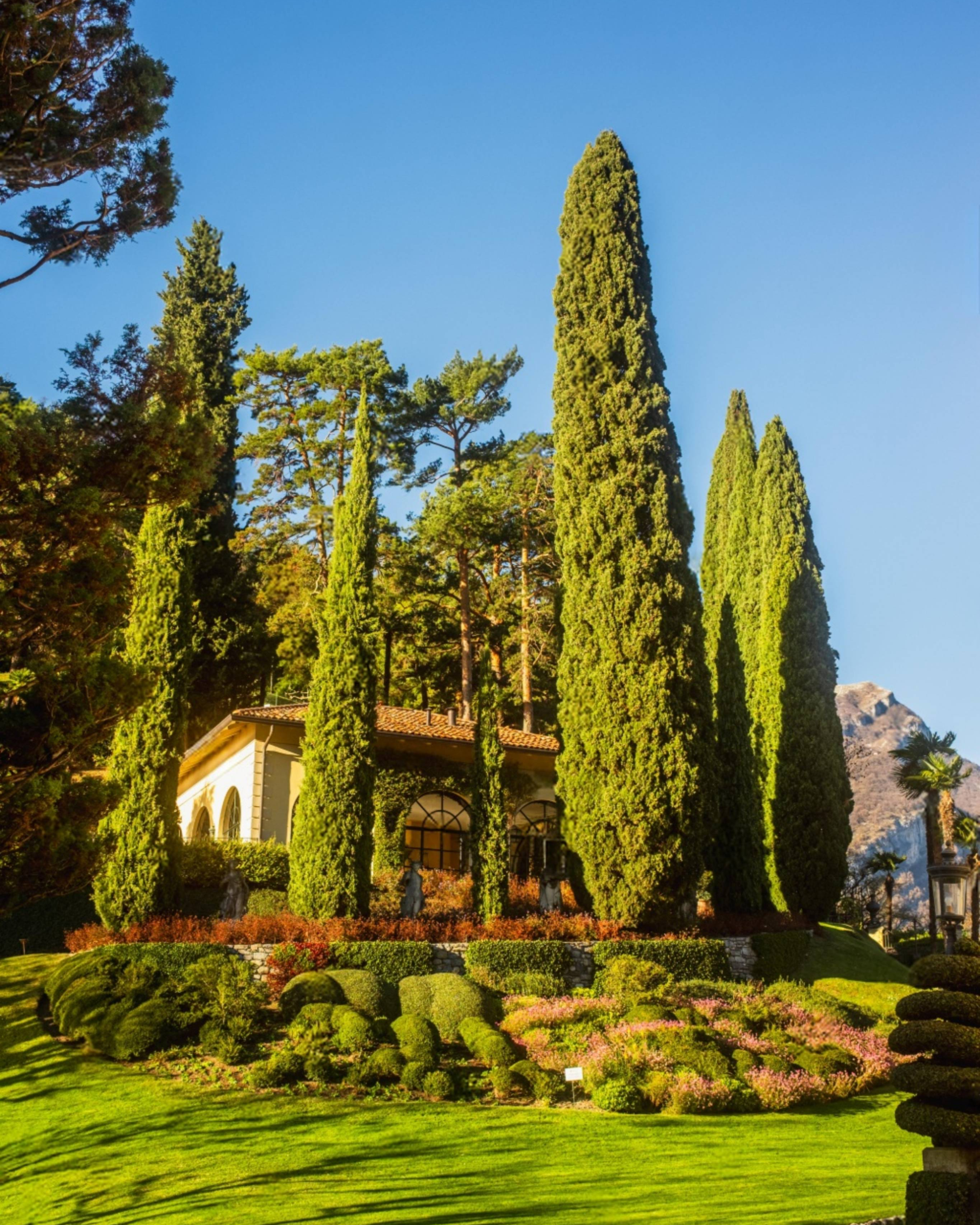 Lush gardens and tall cypress trees surrounding Villa del Balbianello on Lake Como.