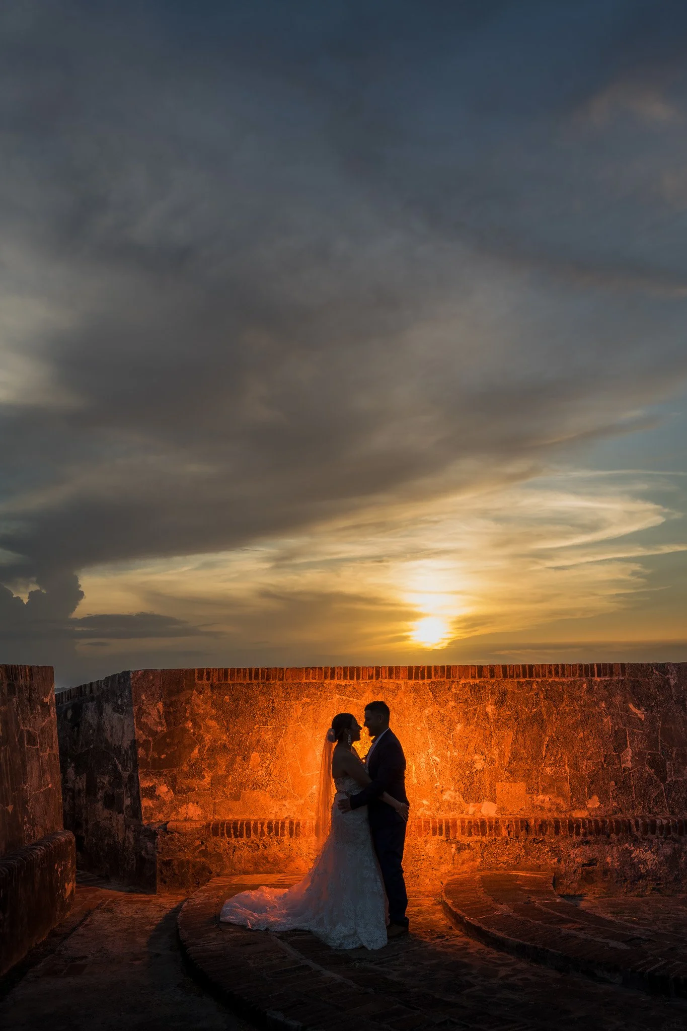 Dramatic sunset silhouette of a bride and groom illuminated against the historic walls of Old San Juan during their luxury Puerto Rico elopement.