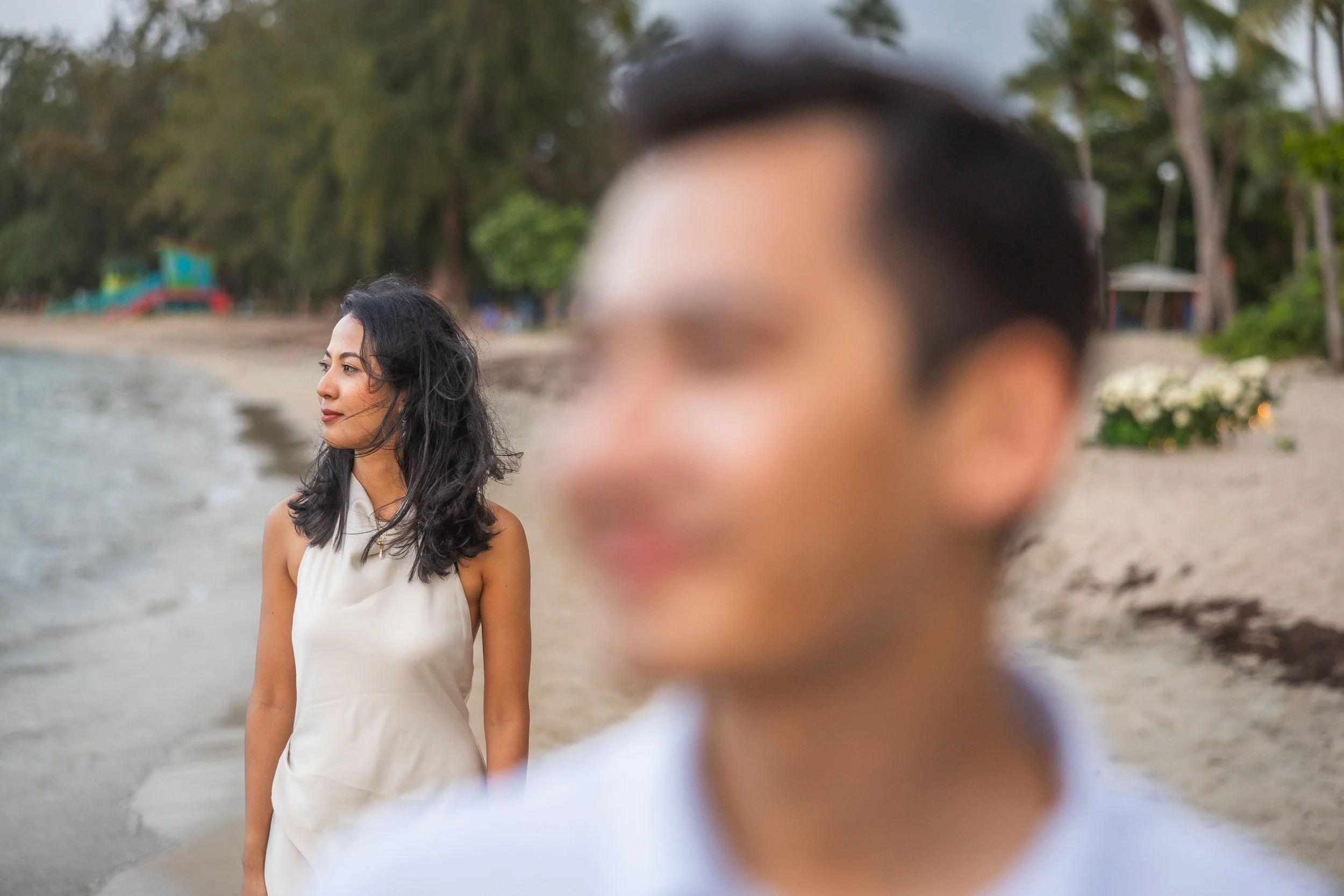 Creative perspective photograph of Sumi standing on the beach as Brijend appears intentionally blurred in the foreground during their Puerto Rico marriage proposal.