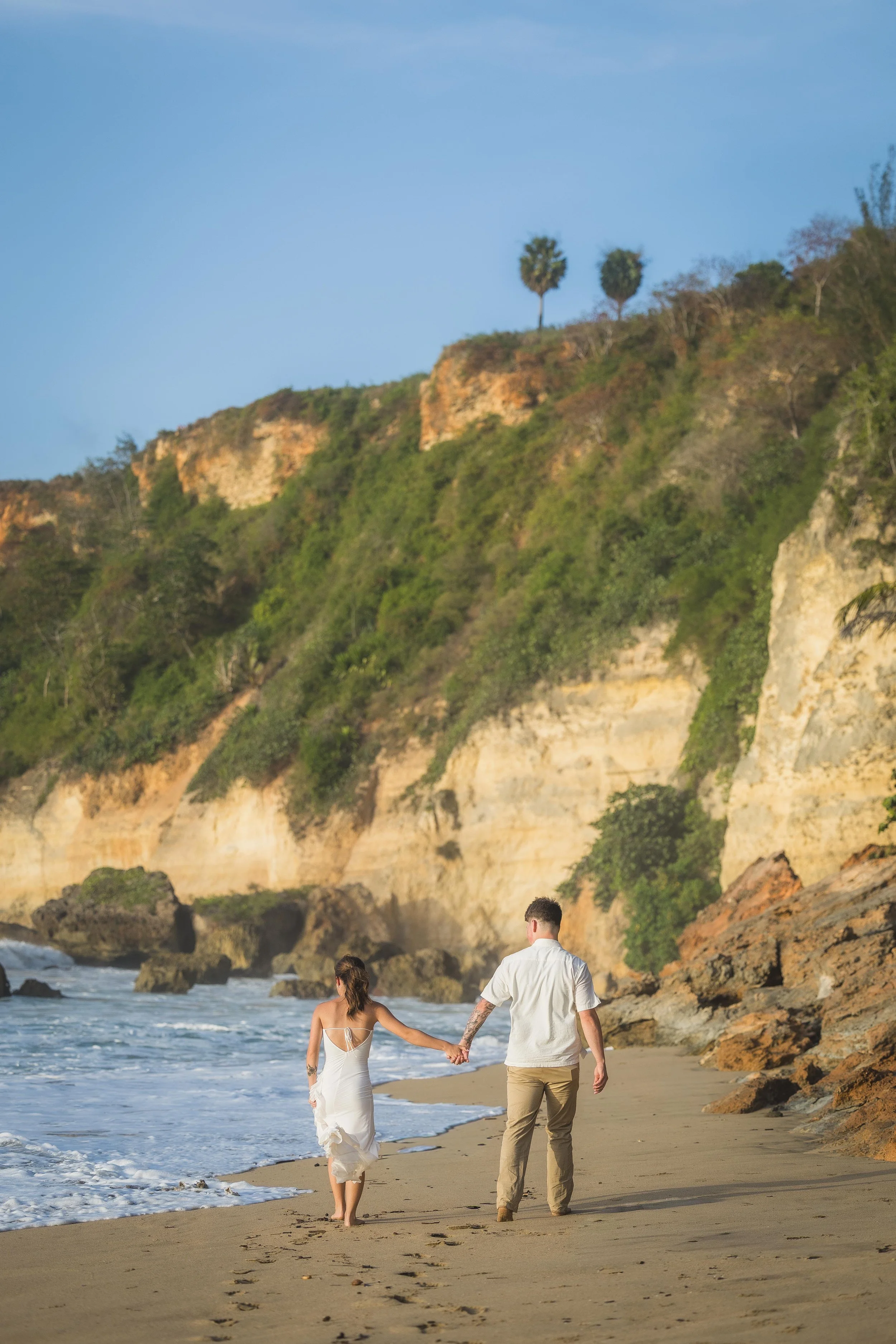 Couple holding hands at Punta Borinquen Beach in Aguadilla, Puerto Rico after their surprise marriage proposal taken by an elopement photographer
