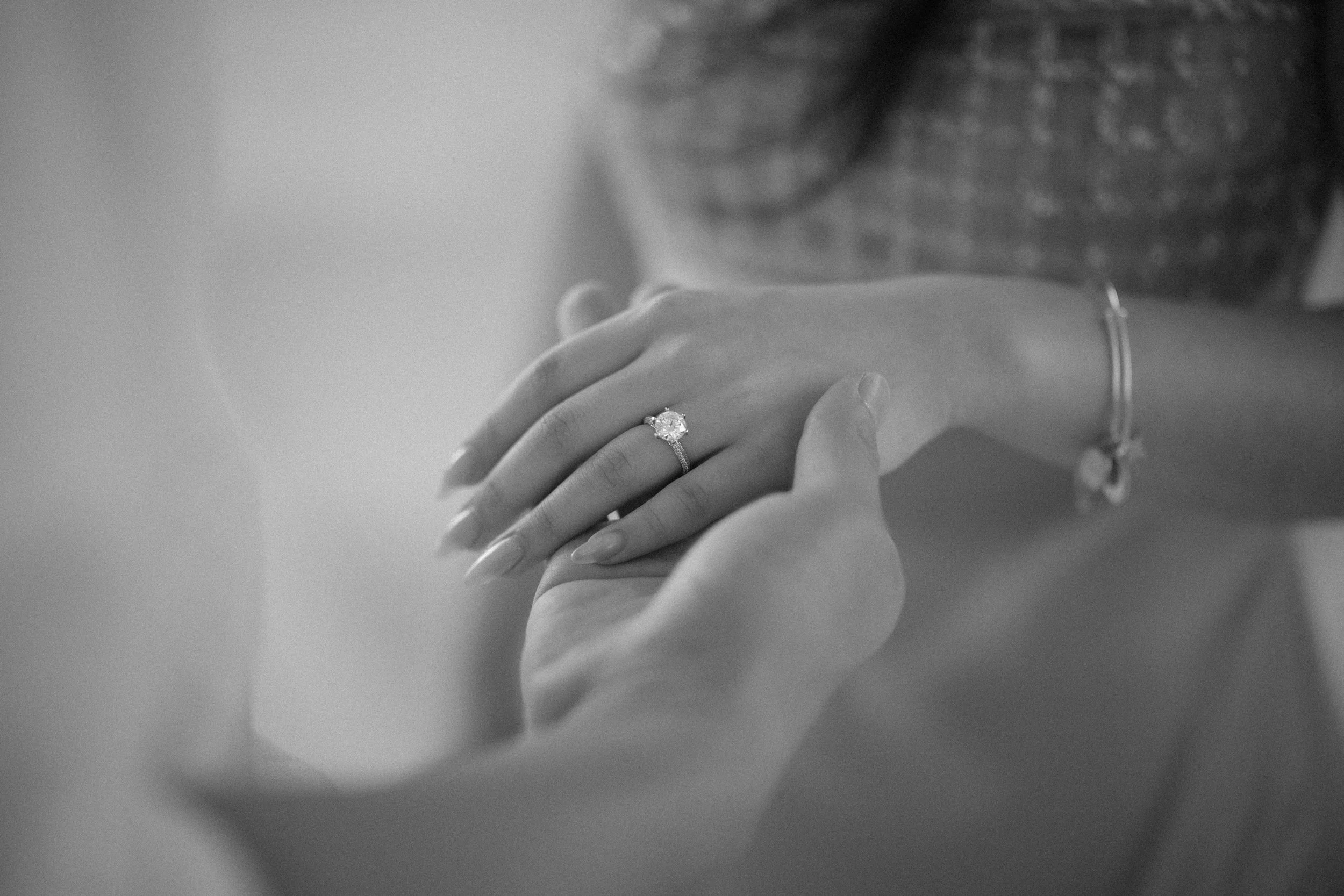 Black-and-white close-up photograph of a newly engaged woman admiring her diamond engagement ring while her fiancé gently holds her hand during a romantic luxury proposal at Hyatt Regency Grand Reserve in Puerto Rico.