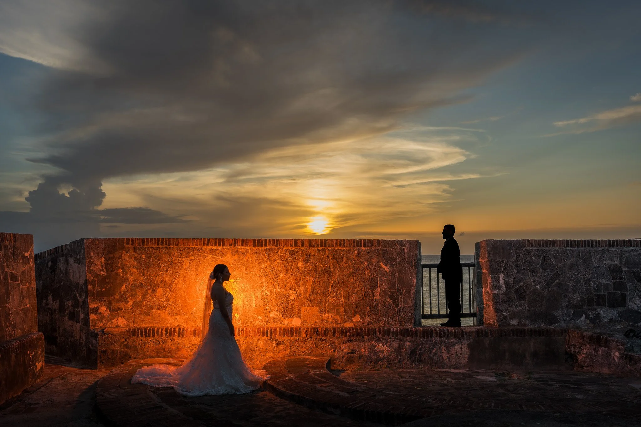 Dramatic sunset silhouette of a bride and groom illuminated against the historic walls of Old San Juan during their luxury Puerto Rico elopement.