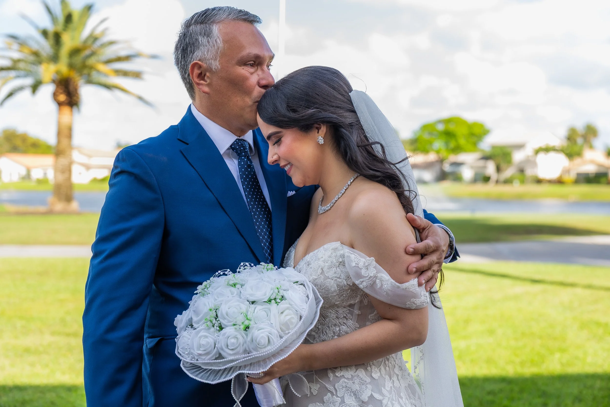 Father kissing bride on forehead after their first look taken by a Miami, Florida wedding photographer at Indian Spring Country Club.