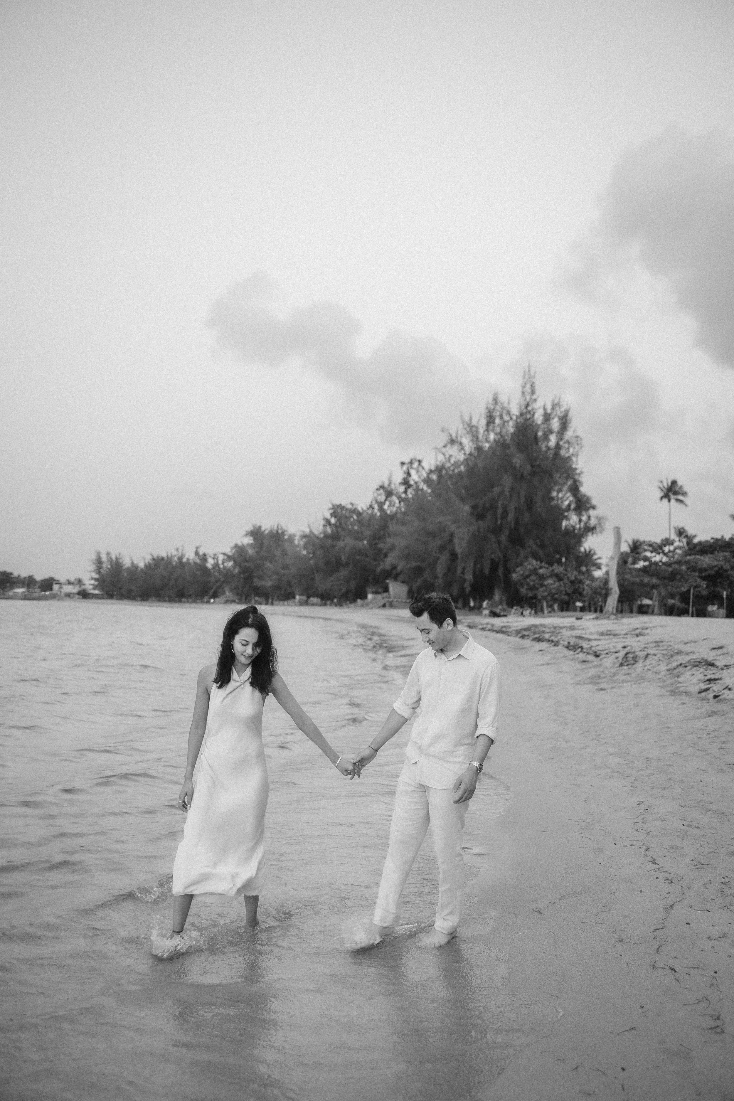 Black and white wide-angle photograph of Brijend and Sumi walking together through the shallow water along a Puerto Rico beach.