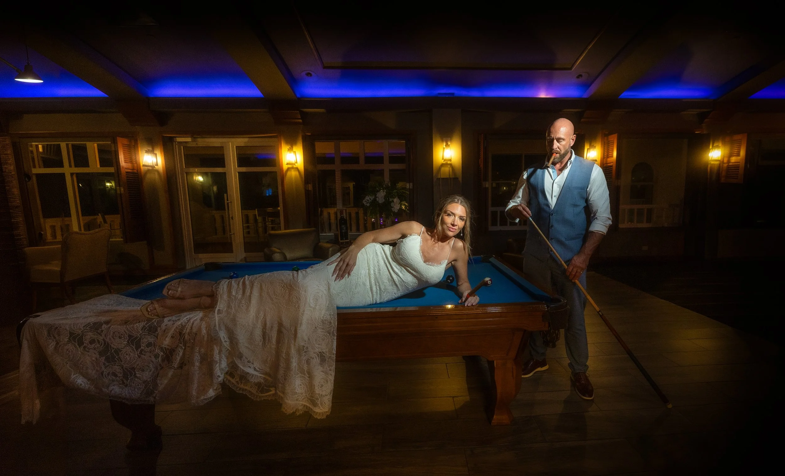 Bride draped over billiard table holding cigar in editorial wedding portrait.