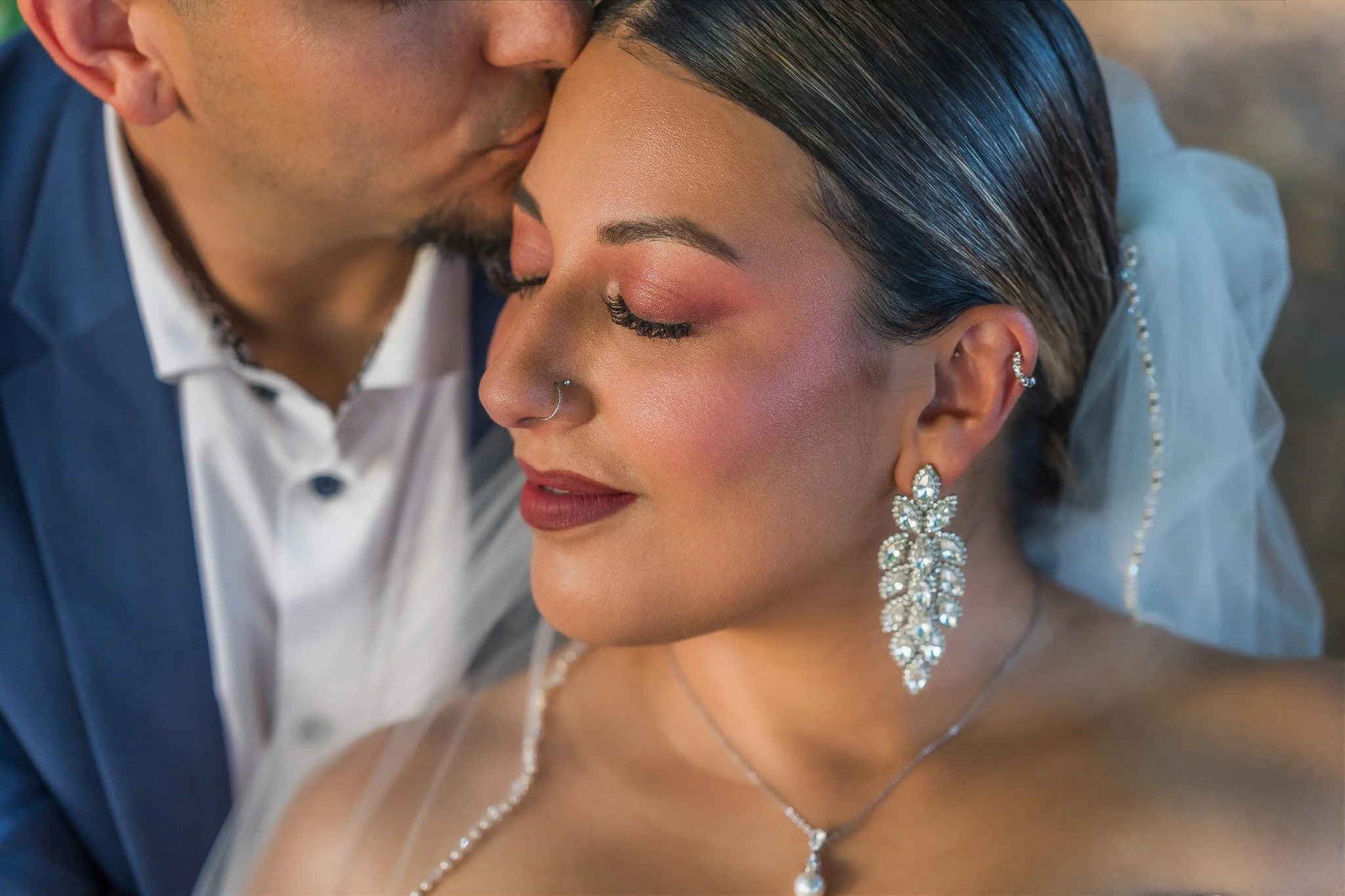 Close-up portrait of the groom kissing the bride's forehead, highlighting elegant bridal makeup, jewelry, and emotion during a Puerto Rico elopement.