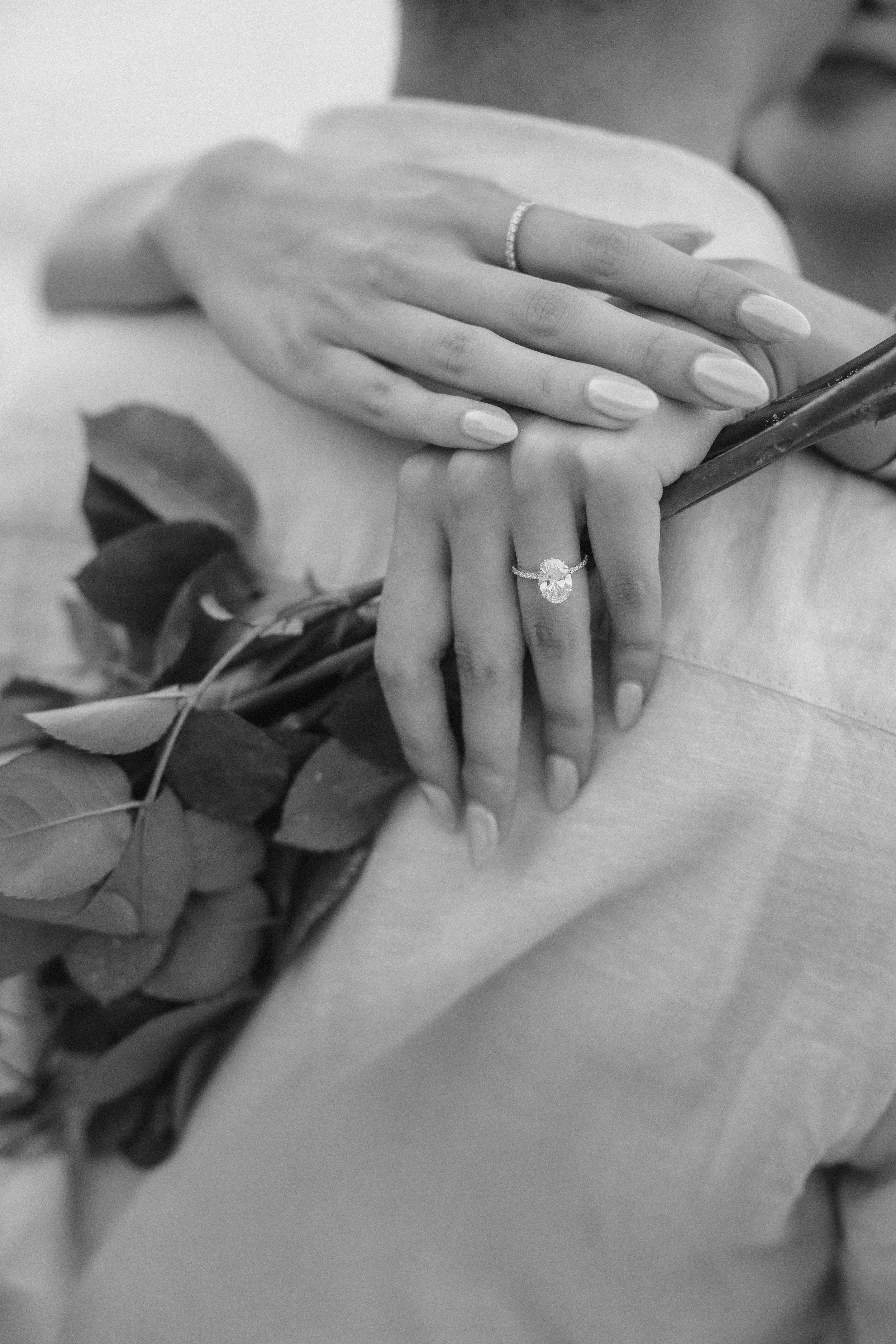 Close-up black and white photograph of Brijend and Sumi’s engagement rings and hands resting together with white roses during their Puerto Rico marriage proposal.