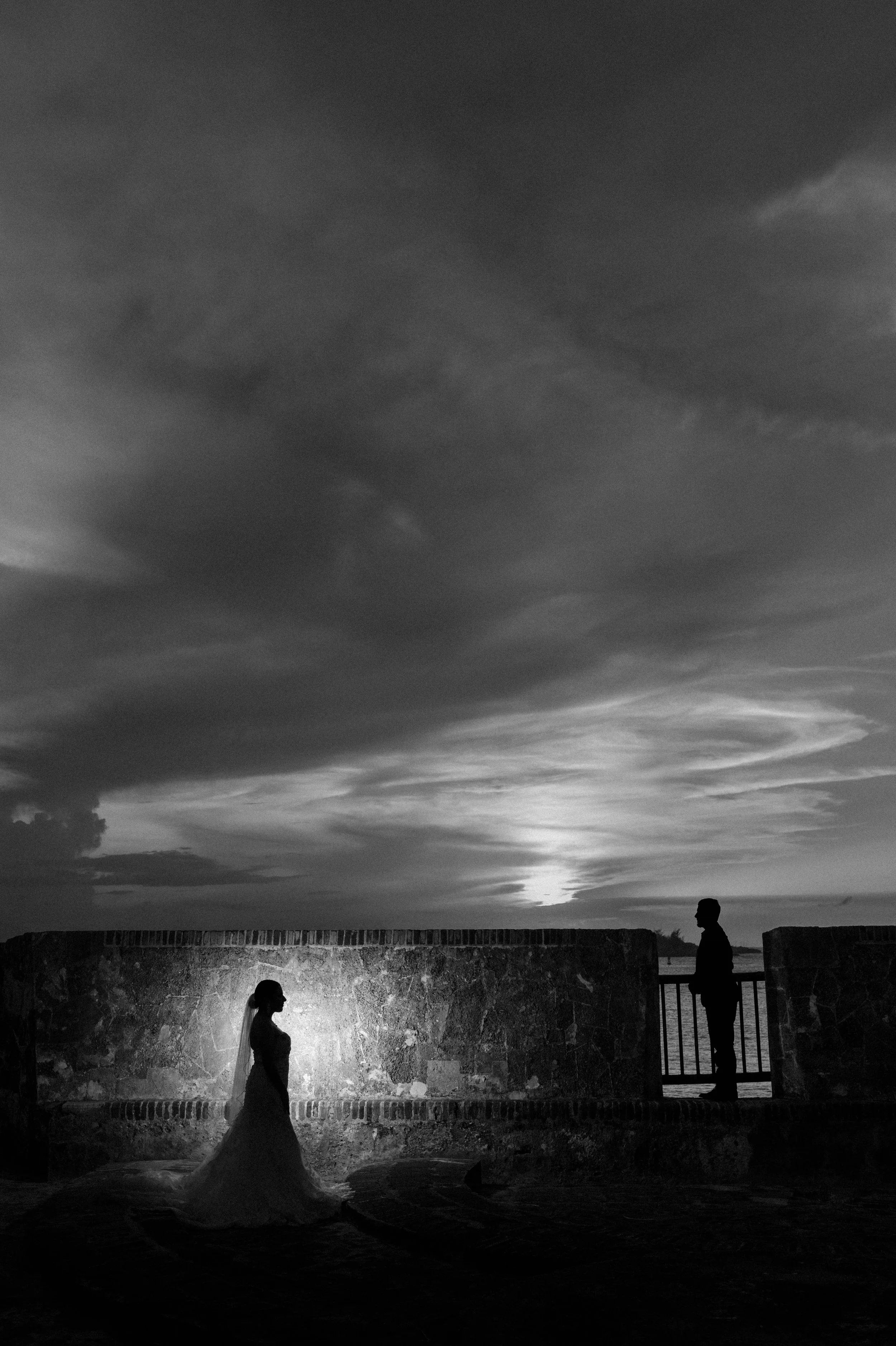 Bride and groom embracing in silhouette against a glowing sunset and historic stone walls during a luxury destination elopement in Old San Juan, Puerto Rico.