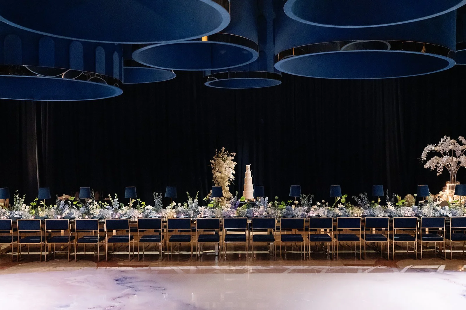 Grand ballroom wedding reception at The Breakers Palm Beach with a navy and gold long table, custom lampshade installation, candlelight, and white floral design.