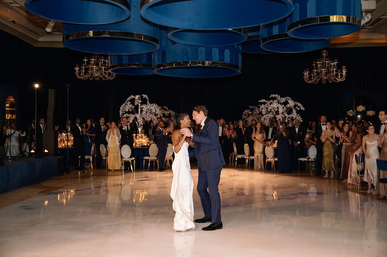 Bride and groom share their first dance in the Venetian Ballroom at The Breakers Palm Beach surrounded by guests, candlelight, and white orchid floral installations.