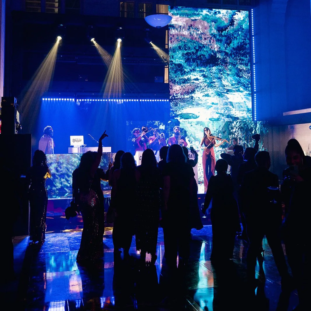 Live orchestra, dramatic lighting, LED wall, and silhouetted guests during a large-scale event production in Miami.