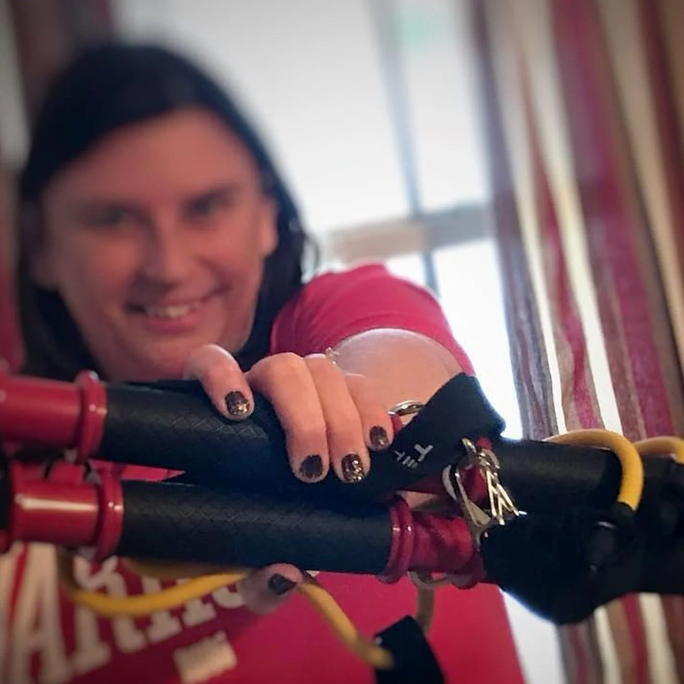A woman with dark hair smiling and leaning forward on her bike handlebars, with a window and curtains in the background.
