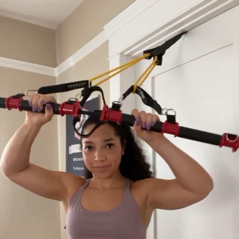 Woman exercising with a resistance and suspension training system attached to the ceiling.