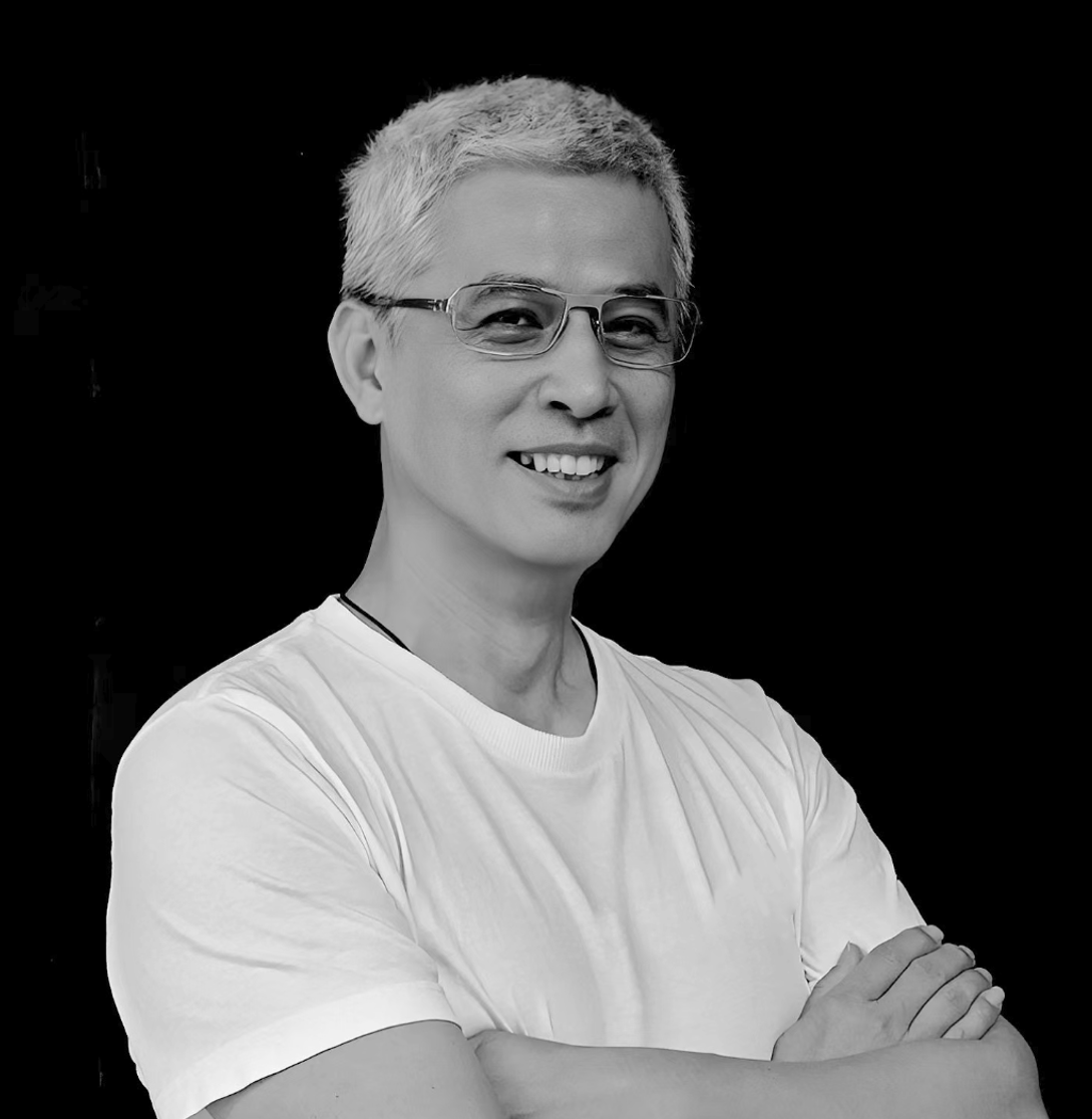 A smiling woman with short gray hair and glasses crossing her arms, wearing a white t-shirt against a black background.