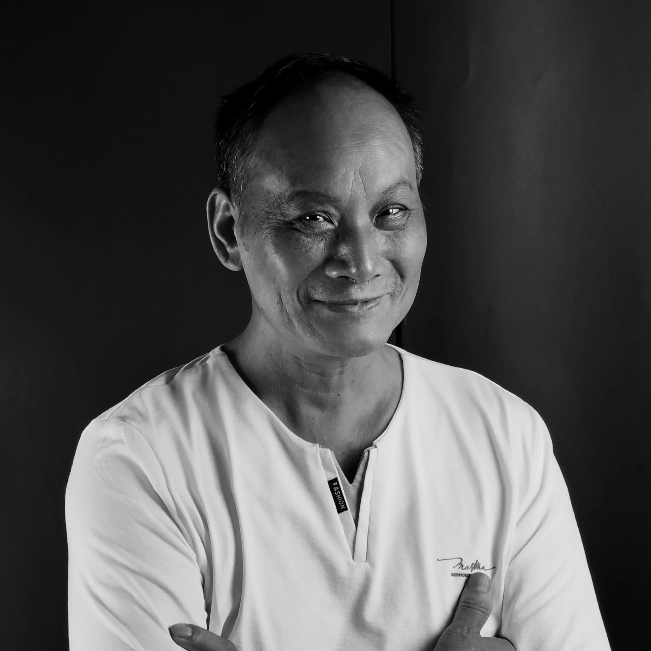 Black and white portrait of a smiling man with short hair, wearing a casual shirt, standing against a plain background.