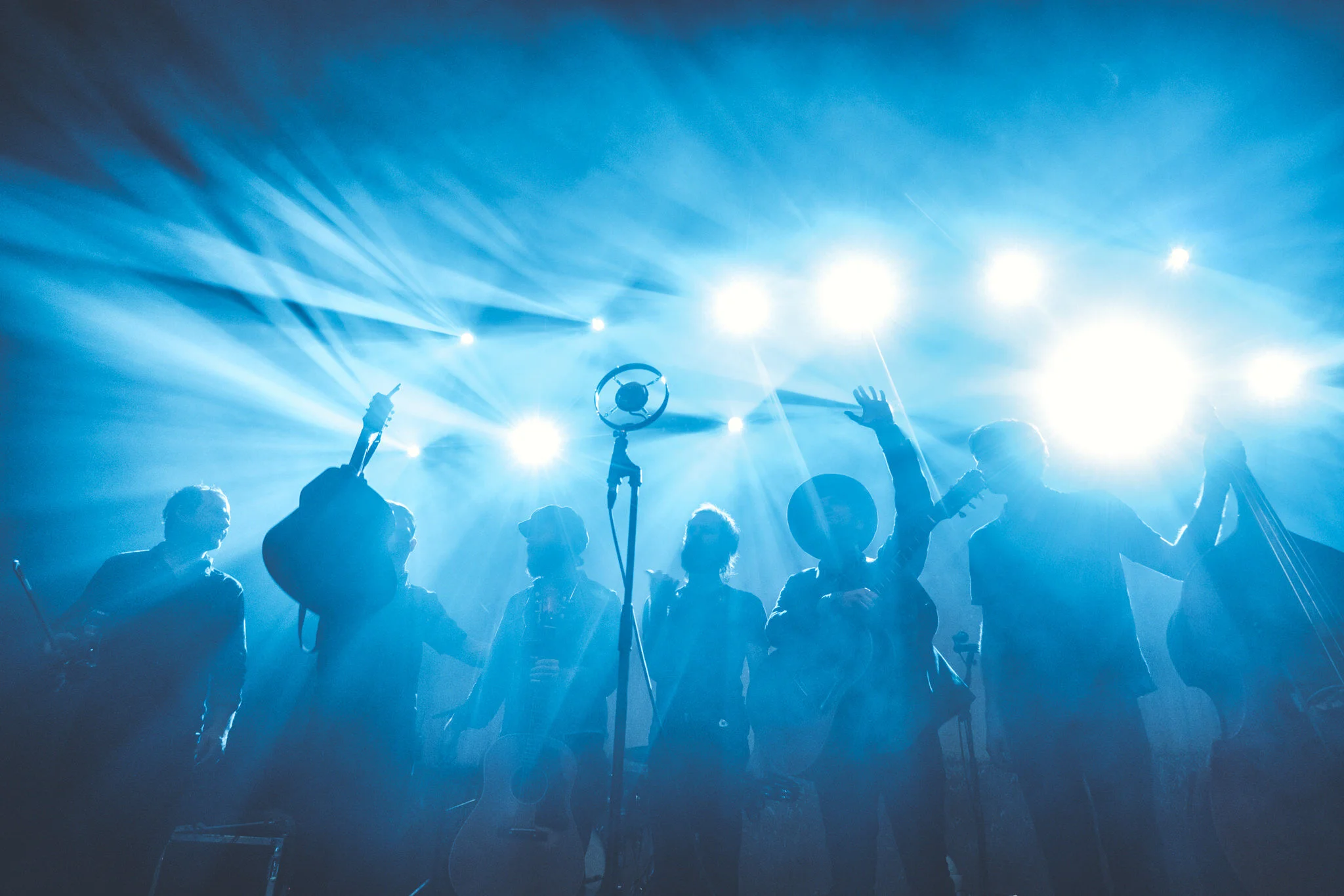 Backlit silhouettes of a band playing musical instruments on stage with bright blue stage lights.