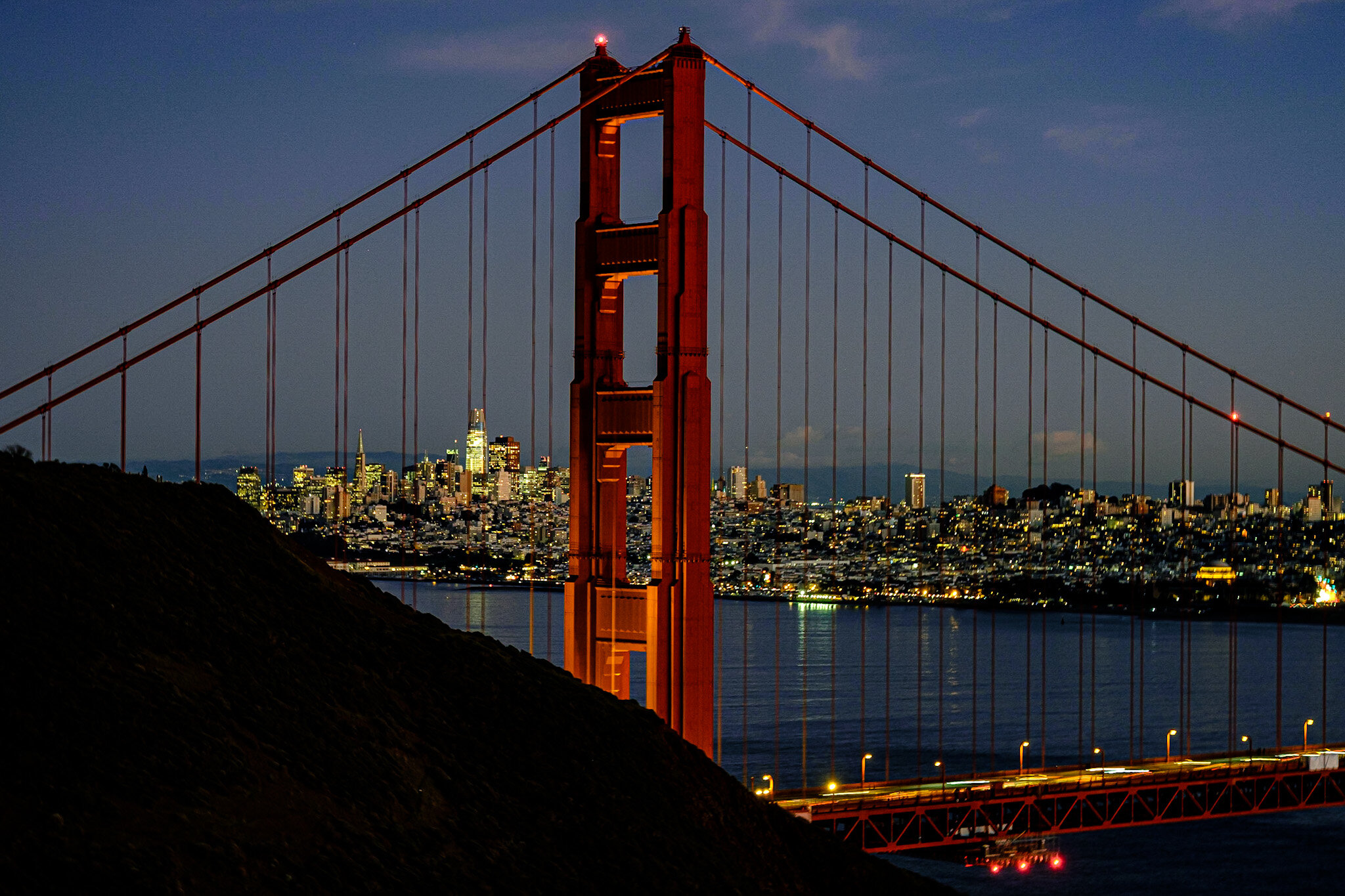 Nighttime view of the illuminated Golden Gate Bridge with the city skyline in the background.