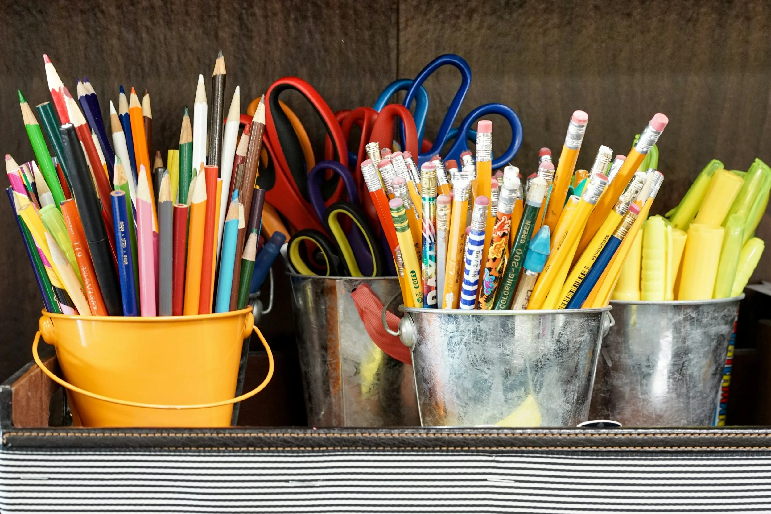 Multiple containers filled with school or office supplies, including colored pencils, markers, scissors, and highlighters.