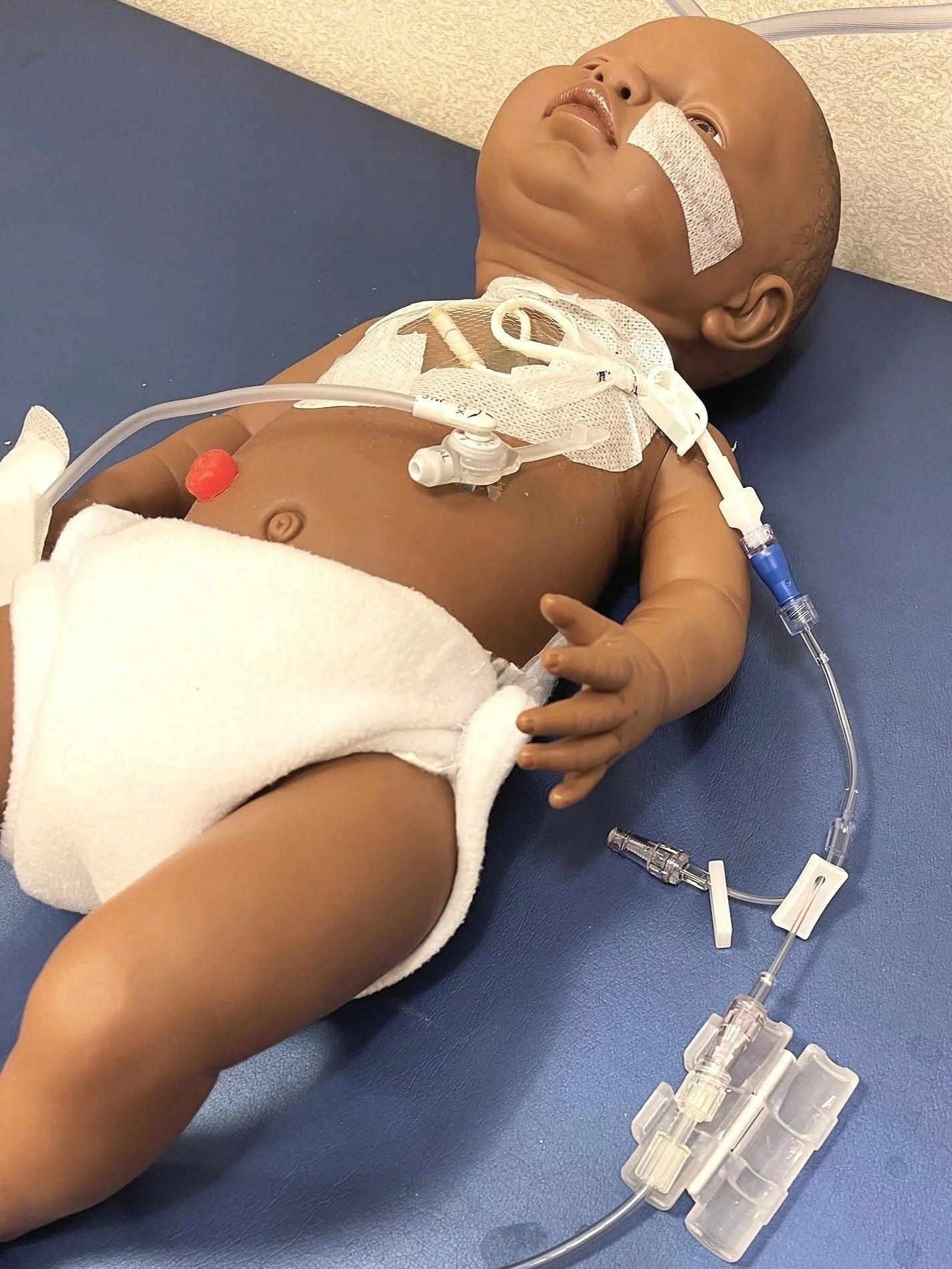 Infant patient with medical tubes and monitoring equipment lying on a hospital bed with connector protector inventions.