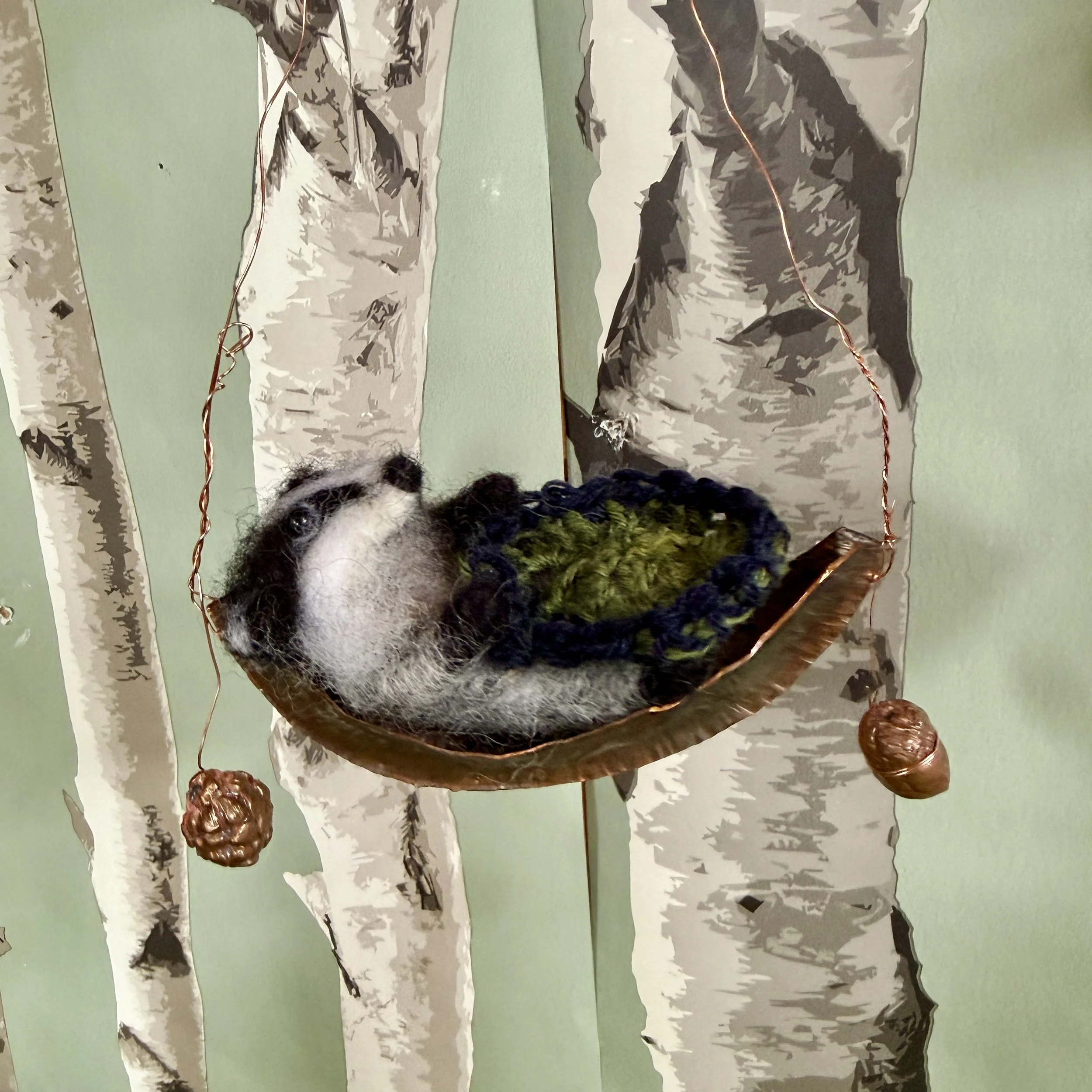 Baby Badger in a copper moon boat crib. Folded hammered copper boat with a cast of a bramble and acorn hanging from each end. £135