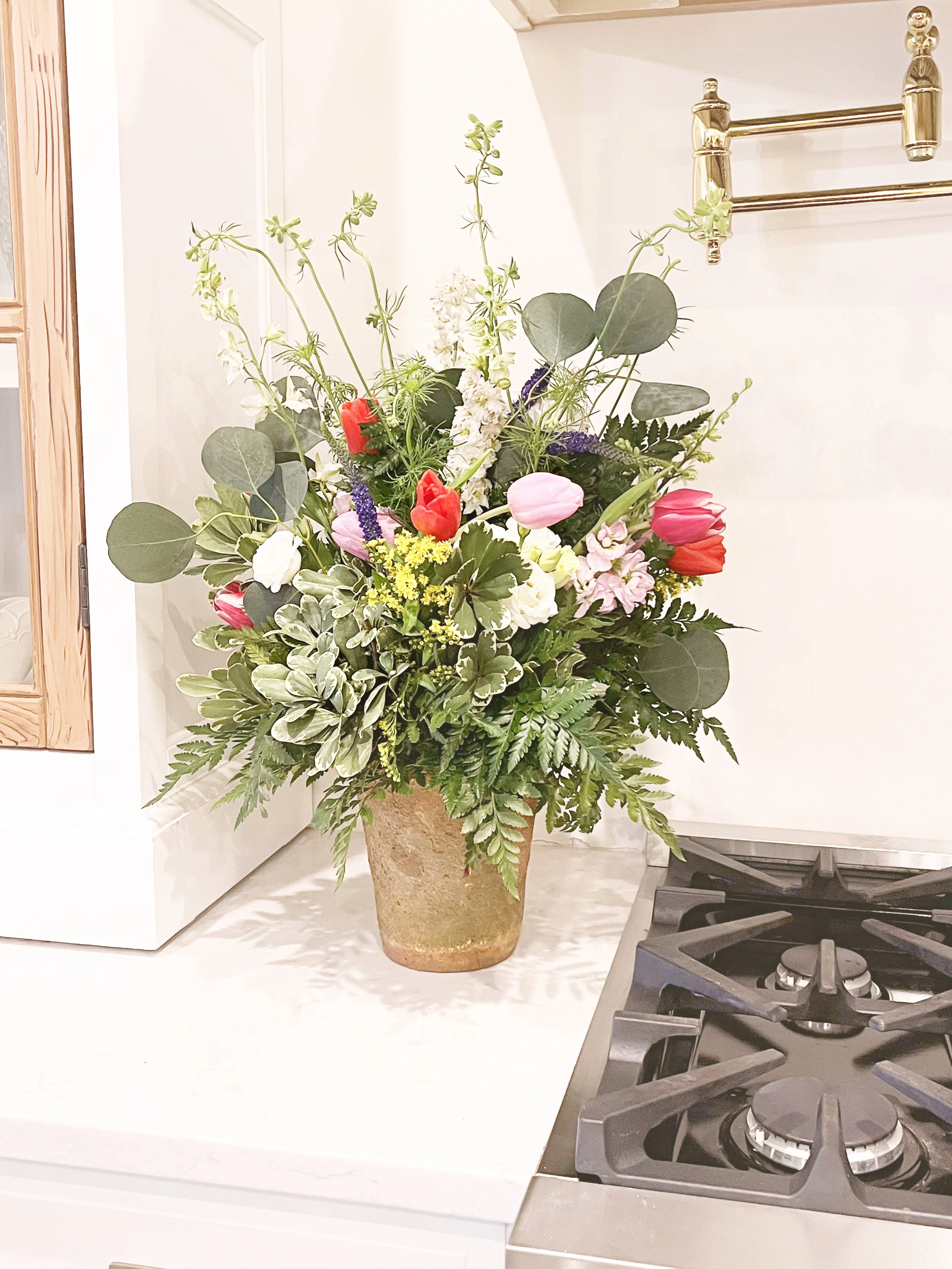 Large Parisian flower shop–inspired floral arrangement in a French terracotta pot featuring tulips, stock, veronica, and solidago in a lush European garden style.